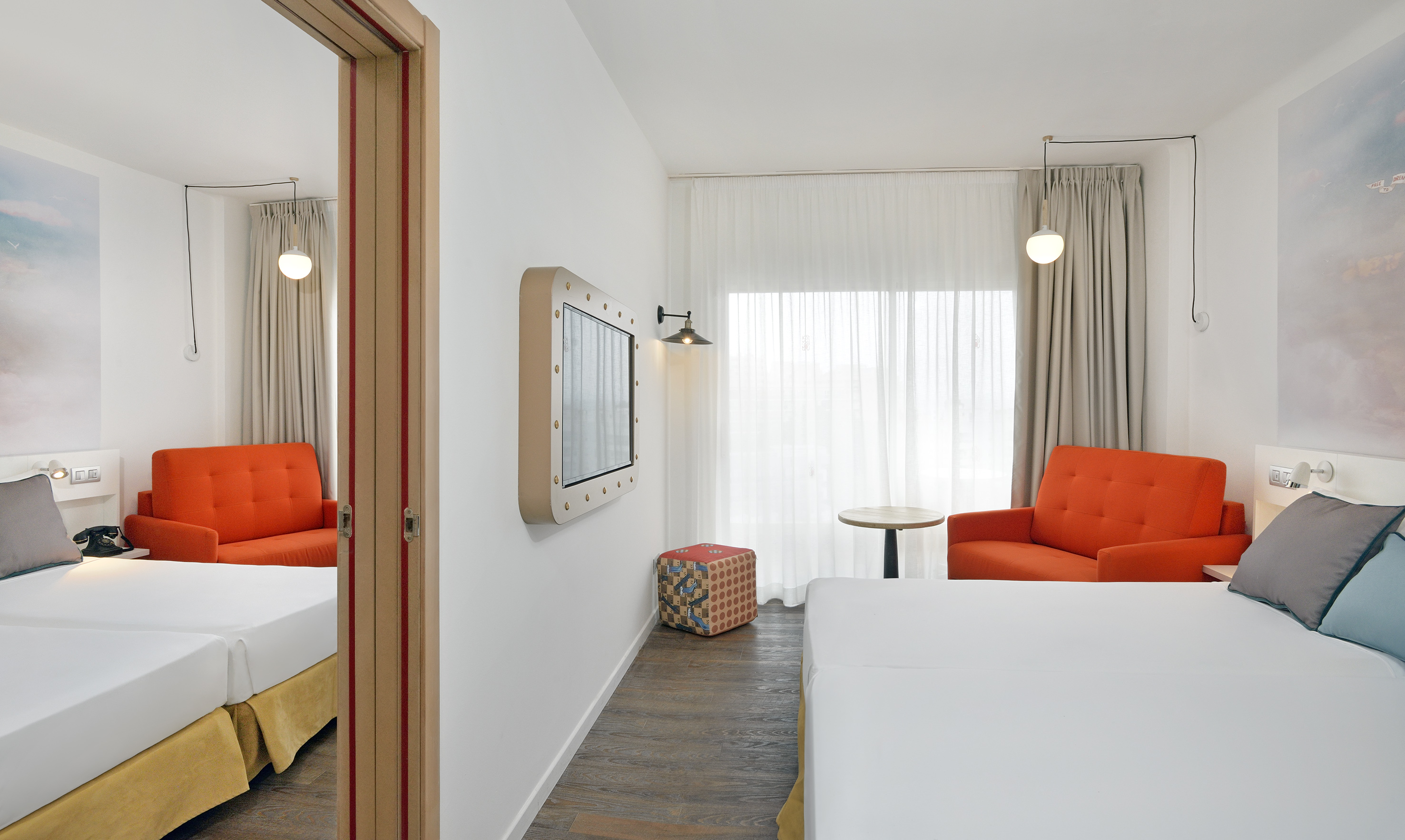 Modern hotel twin room with white beds, orange armchairs, and a porthole TV.