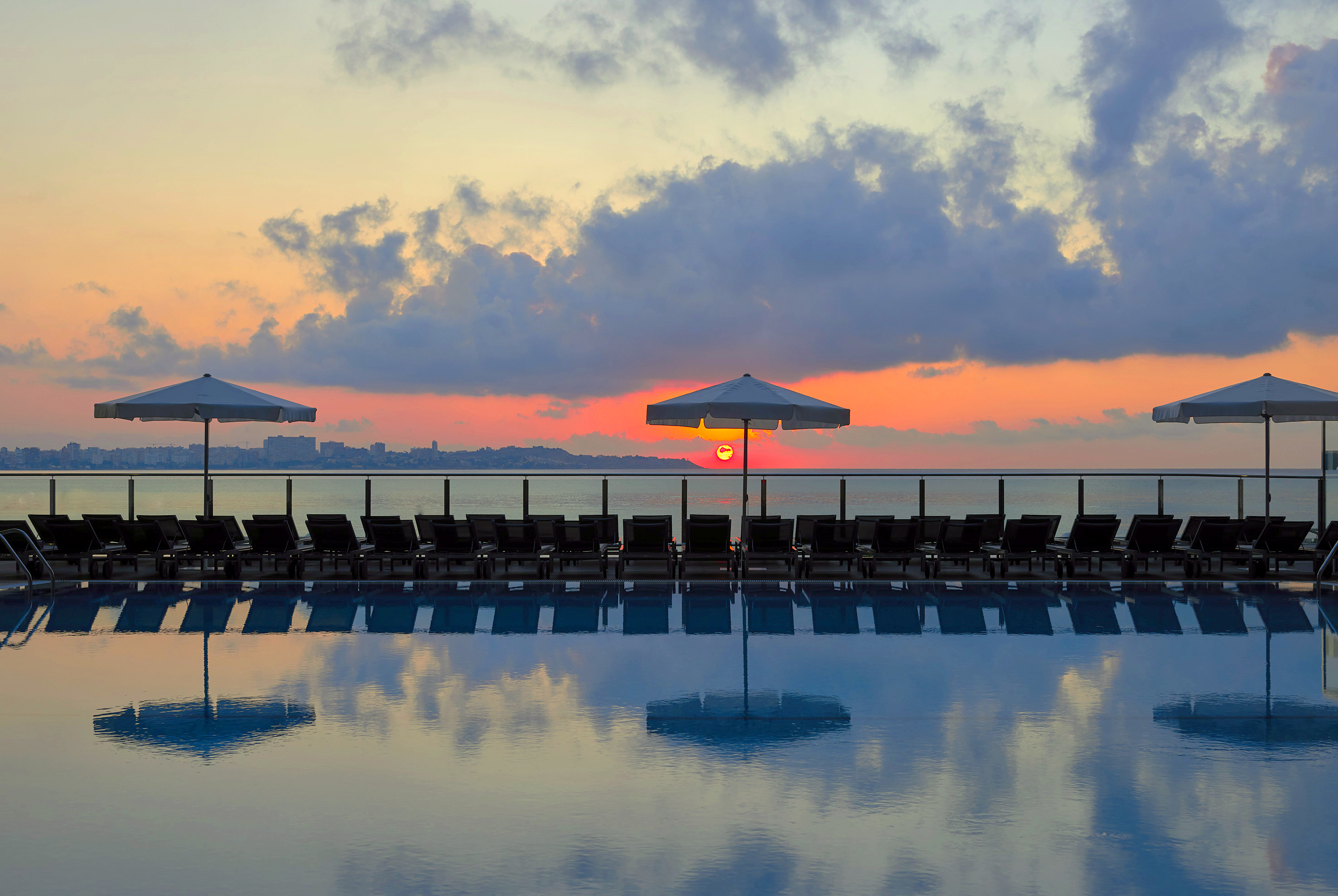 Resort pool with lounge chairs and umbrellas, vibrant ocean sunrise.