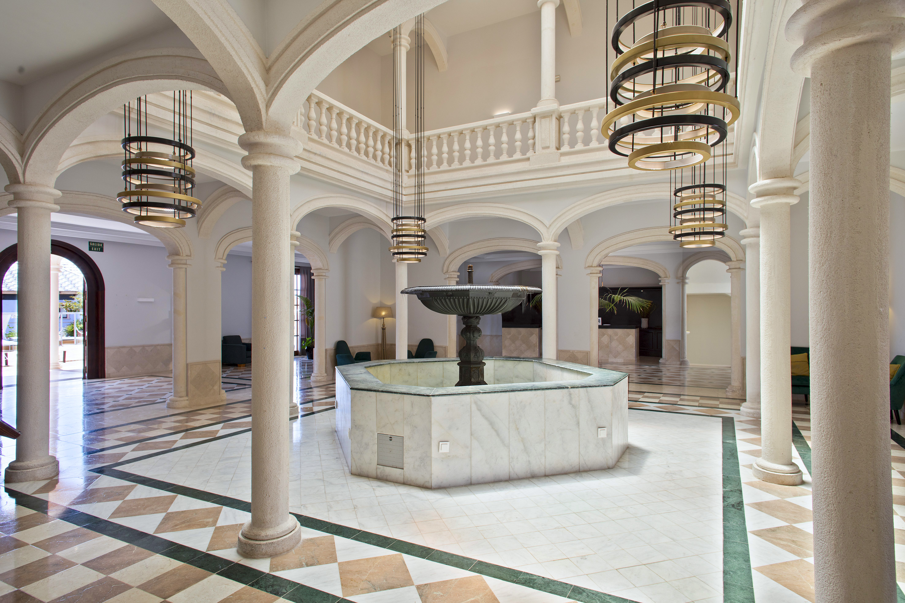 Grand hotel lobby with marble fountain, arched columns, and modern chandeliers.