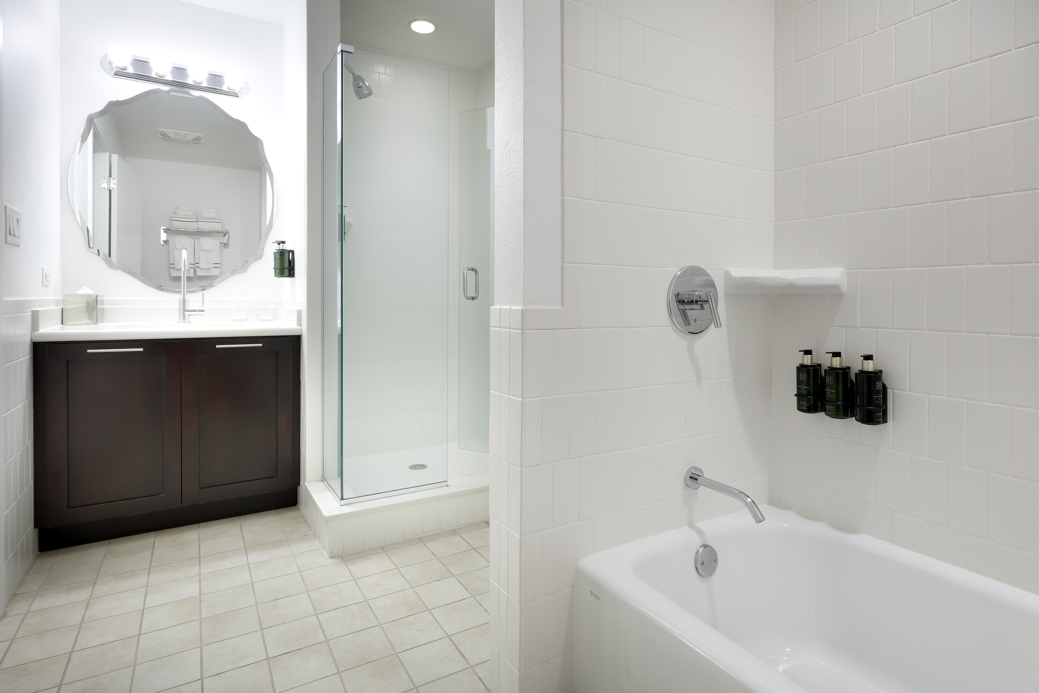 Modern hotel bathroom with white tiles, dark vanity, walk-in shower, and bathtub. - Two-Bedroom Family Suite - Meliá Orlando Celebration, Orlando