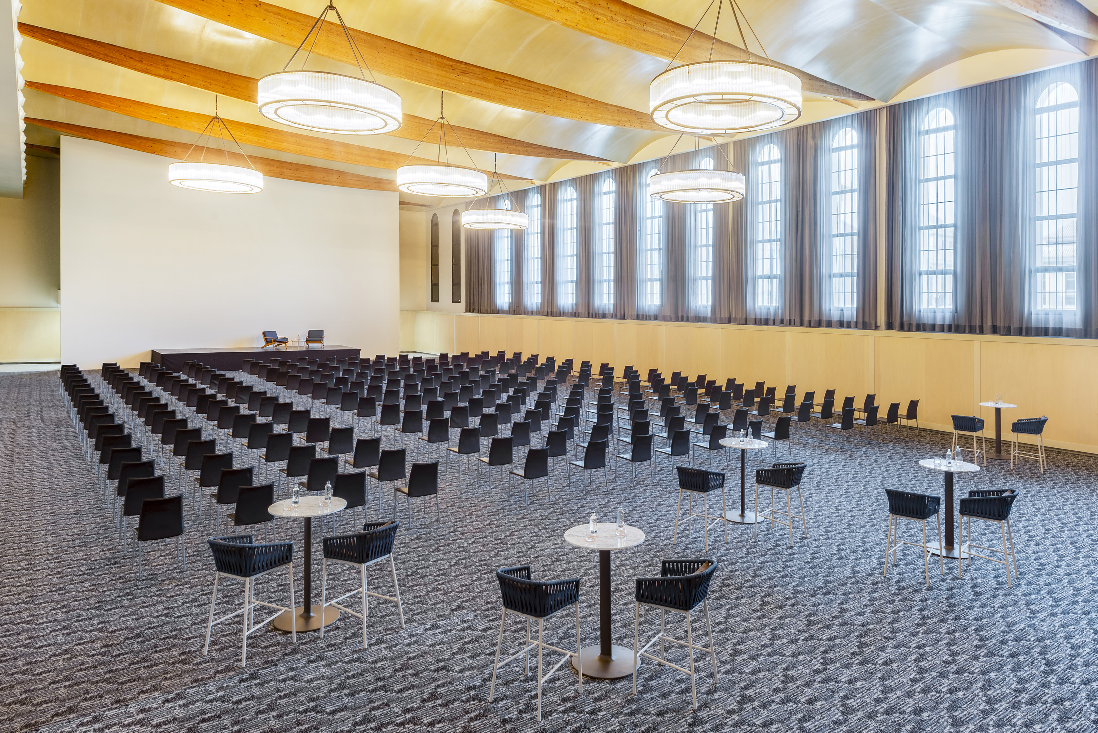 Spacious event hall with theater seating, stage, high tables, chandeliers.