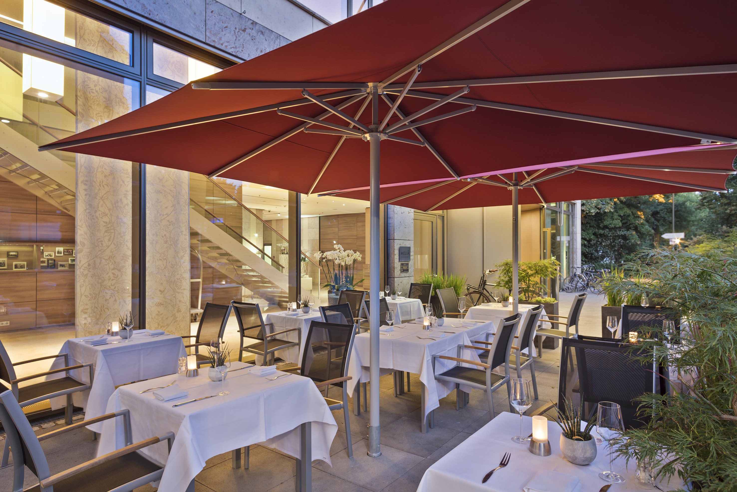 Outdoor restaurant terrace with red umbrellas, set tables, and ambient lighting.