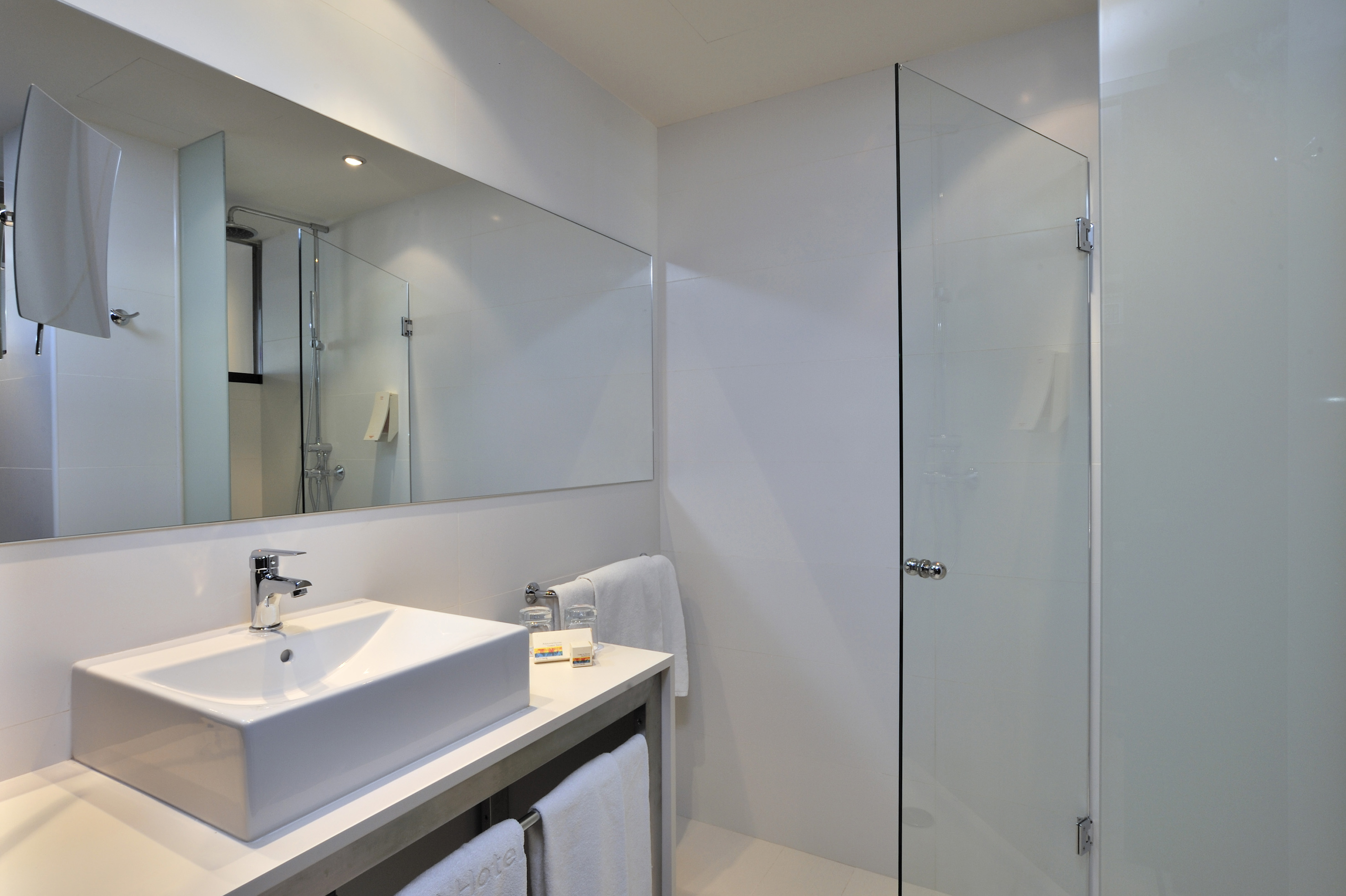 Modern white hotel bathroom with vessel sink, large mirror, and glass shower.