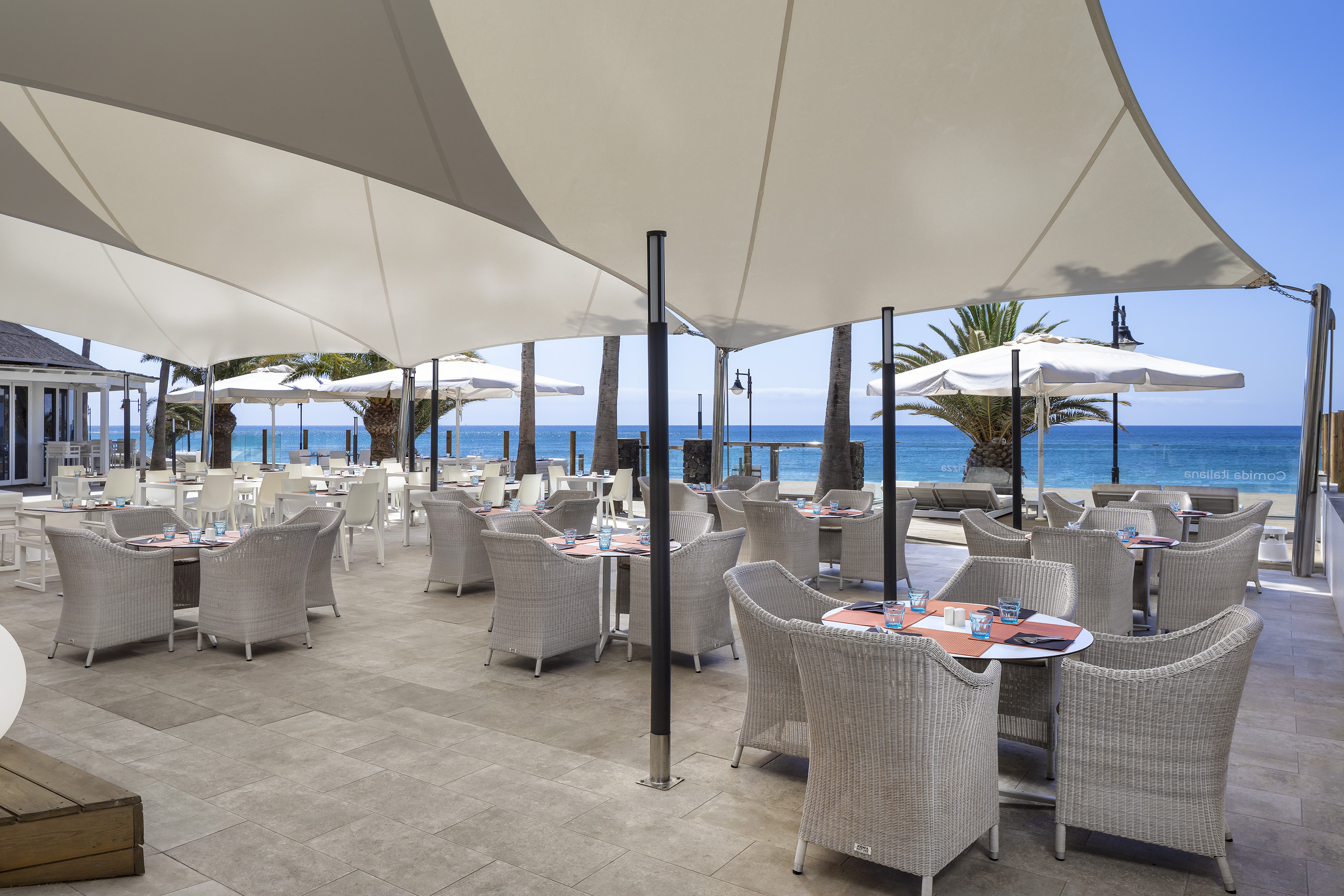 Beachfront outdoor dining with white shade canopies, tables, and ocean view.