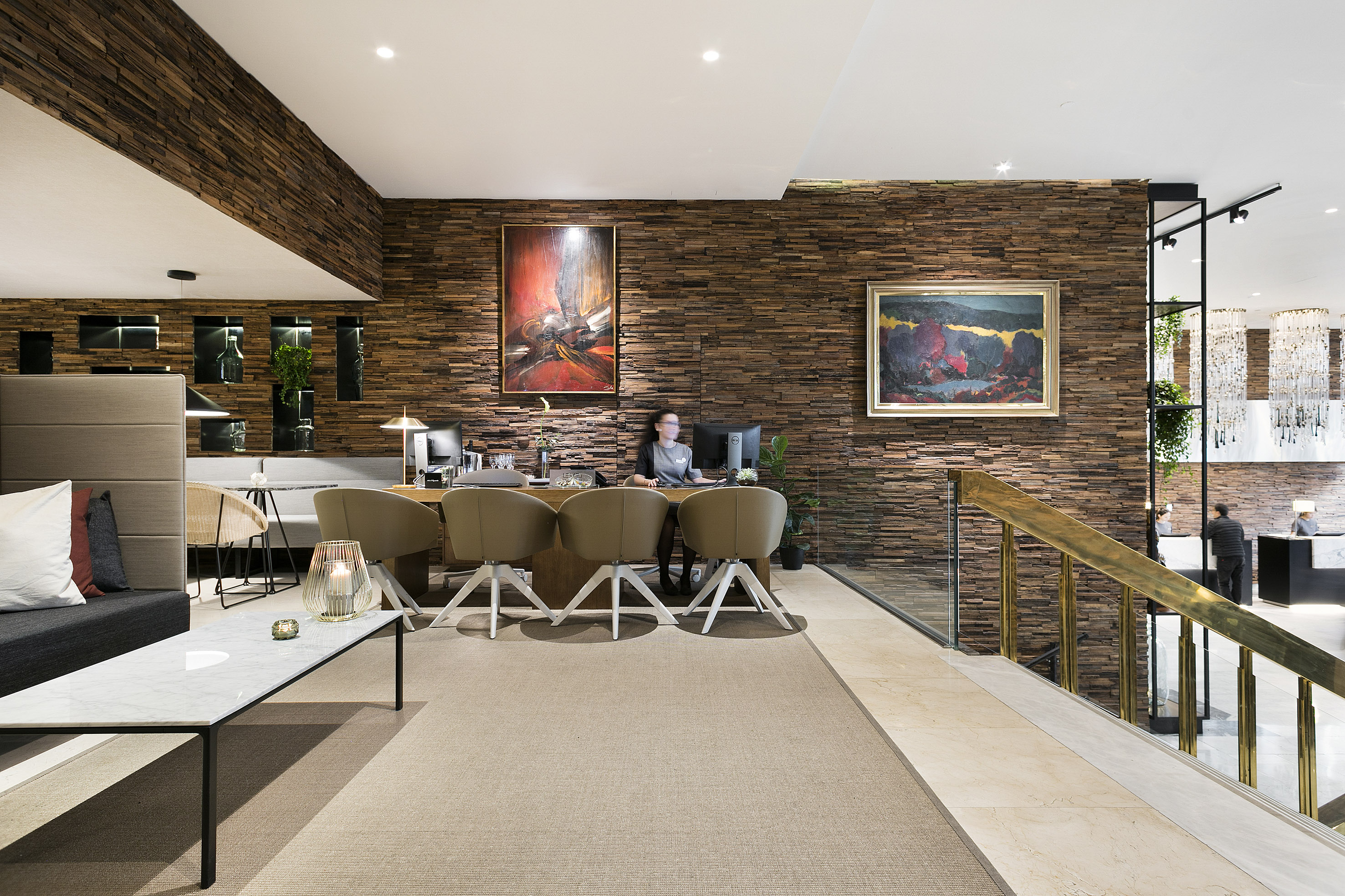 Modern hotel lobby reception with wood paneled walls, abstract art, and lounge seating.