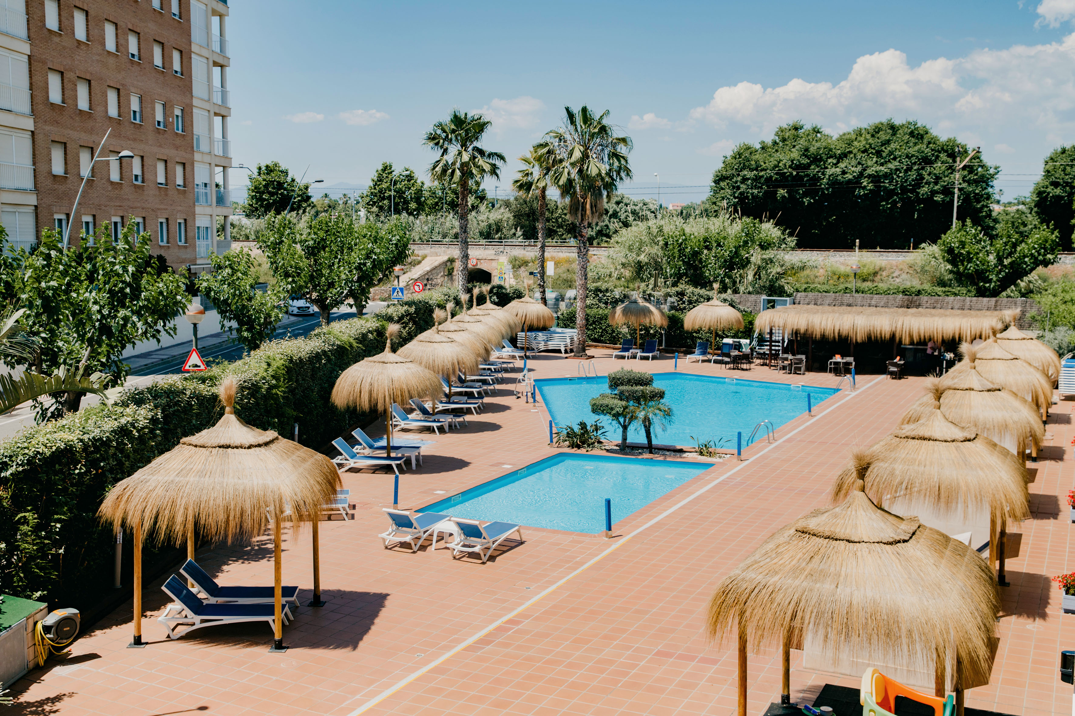 Sunny resort pools with thatched umbrellas, lounge chairs, and palm trees.