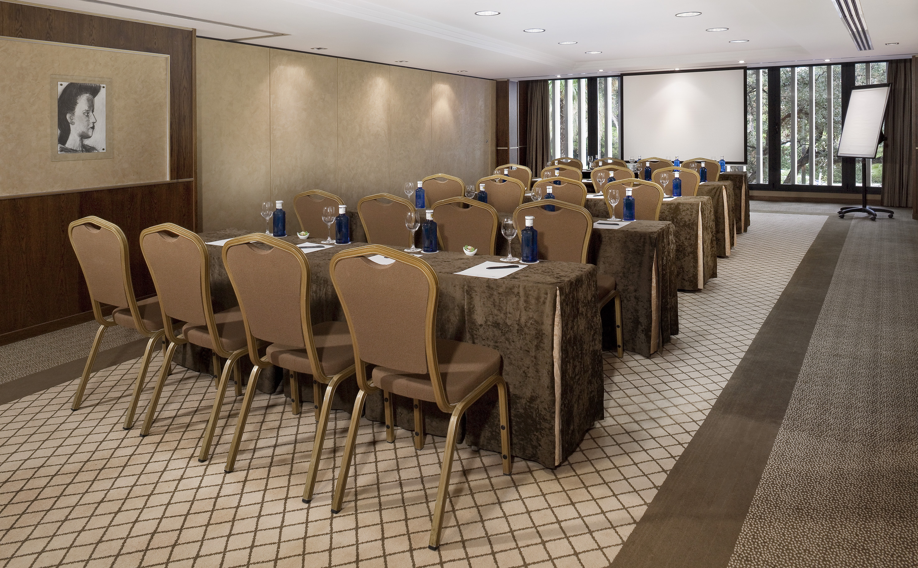 Well-lit meeting room with rows of brown tables, chairs, and a projector screen.