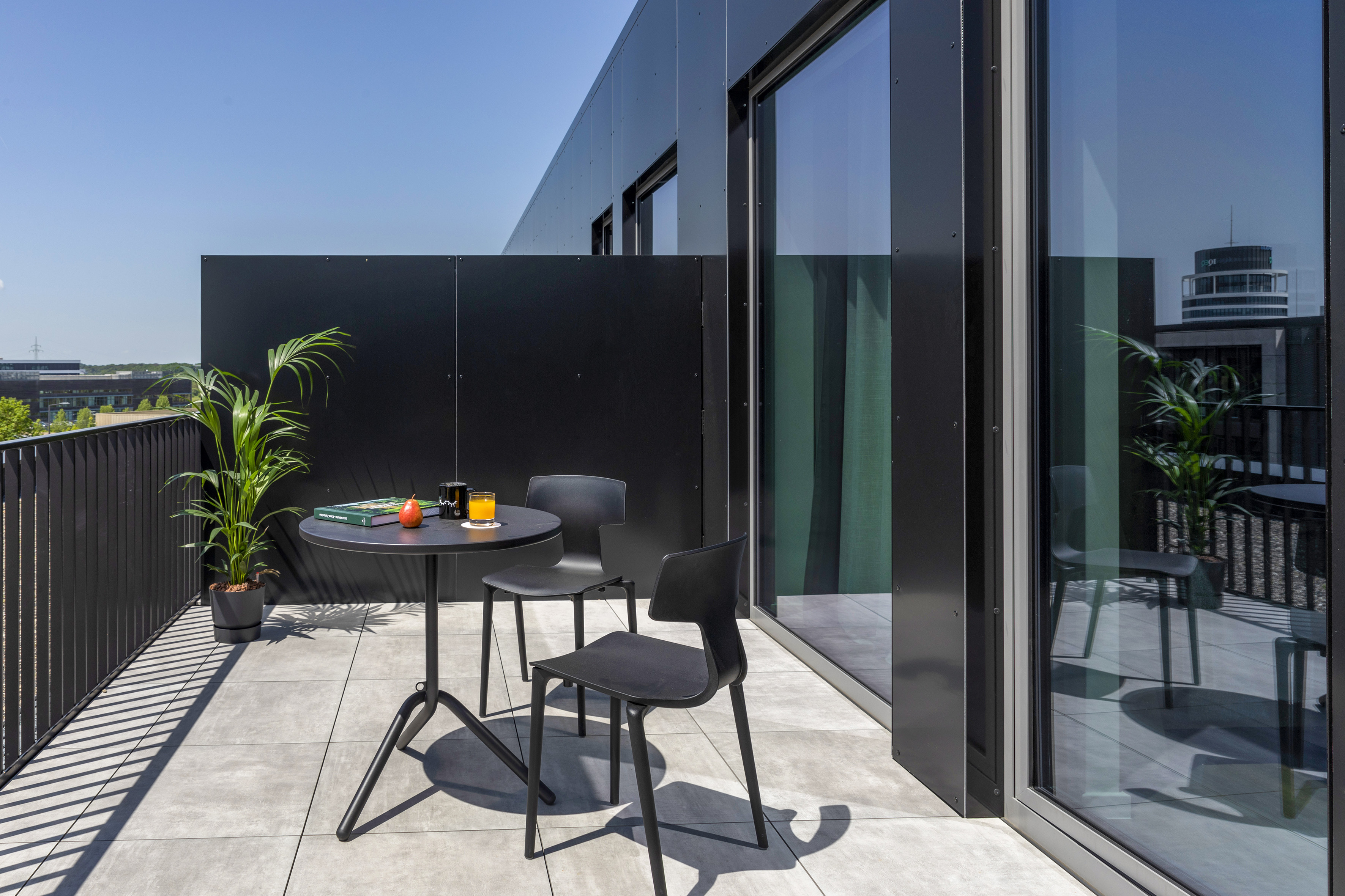 Modern balcony with black outdoor furniture, potted plant, and city view. - The Townhouse - INNSiDE Luxembourg, Luxemburg