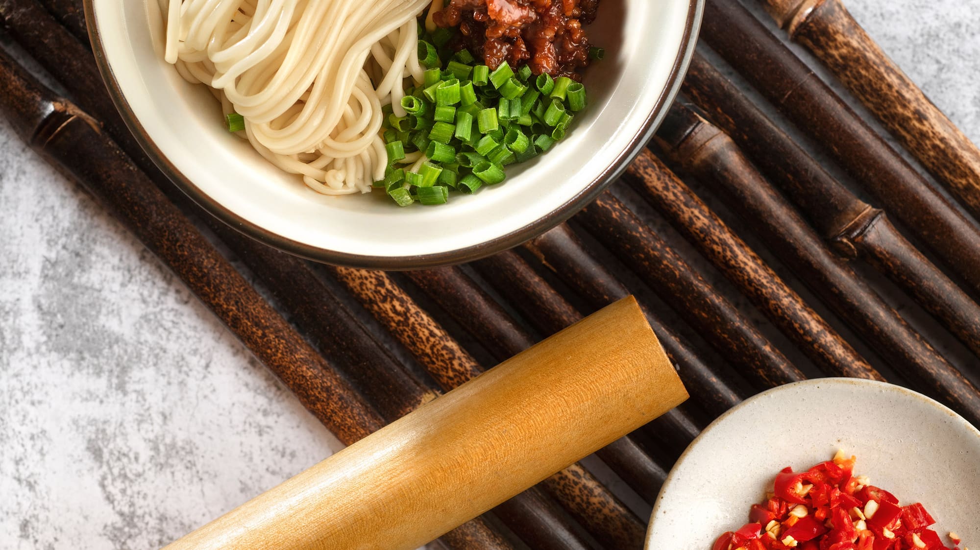 a bowl of noodles and vegetables on a bamboo mat