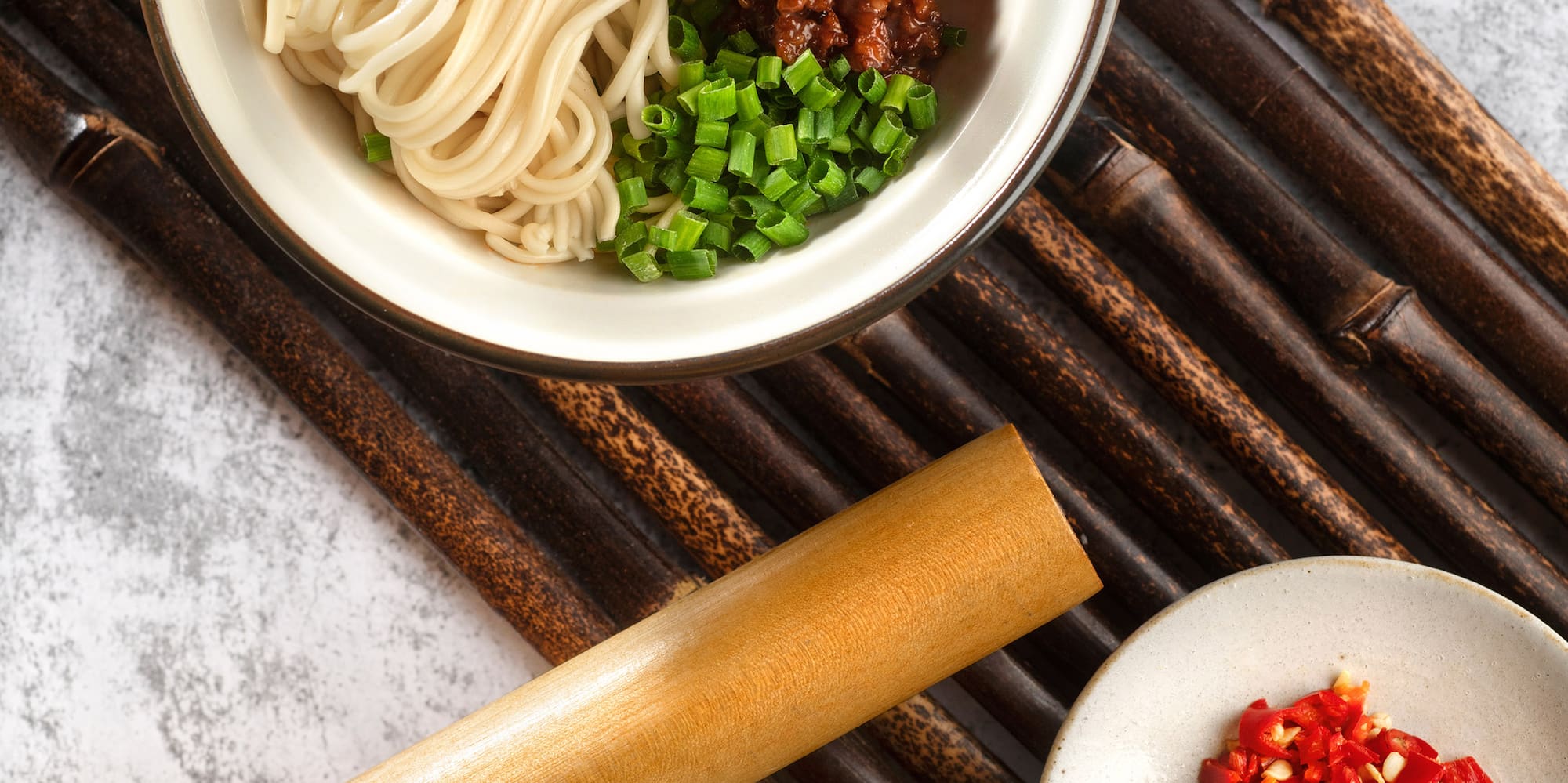 a bowl of noodles and vegetables on a bamboo mat