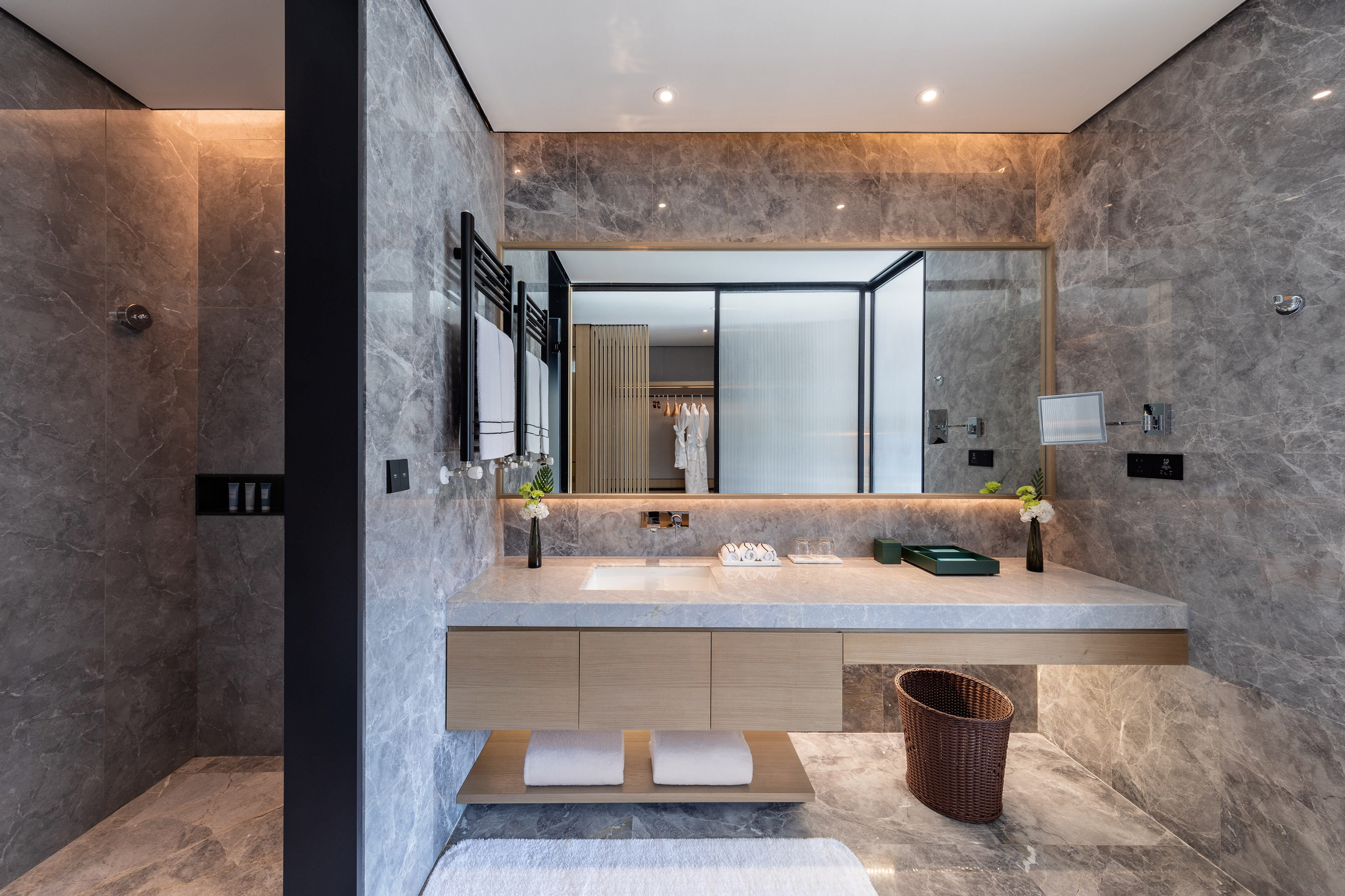 Modern hotel bathroom with gray marble, floating wood vanity, and walk-in shower.