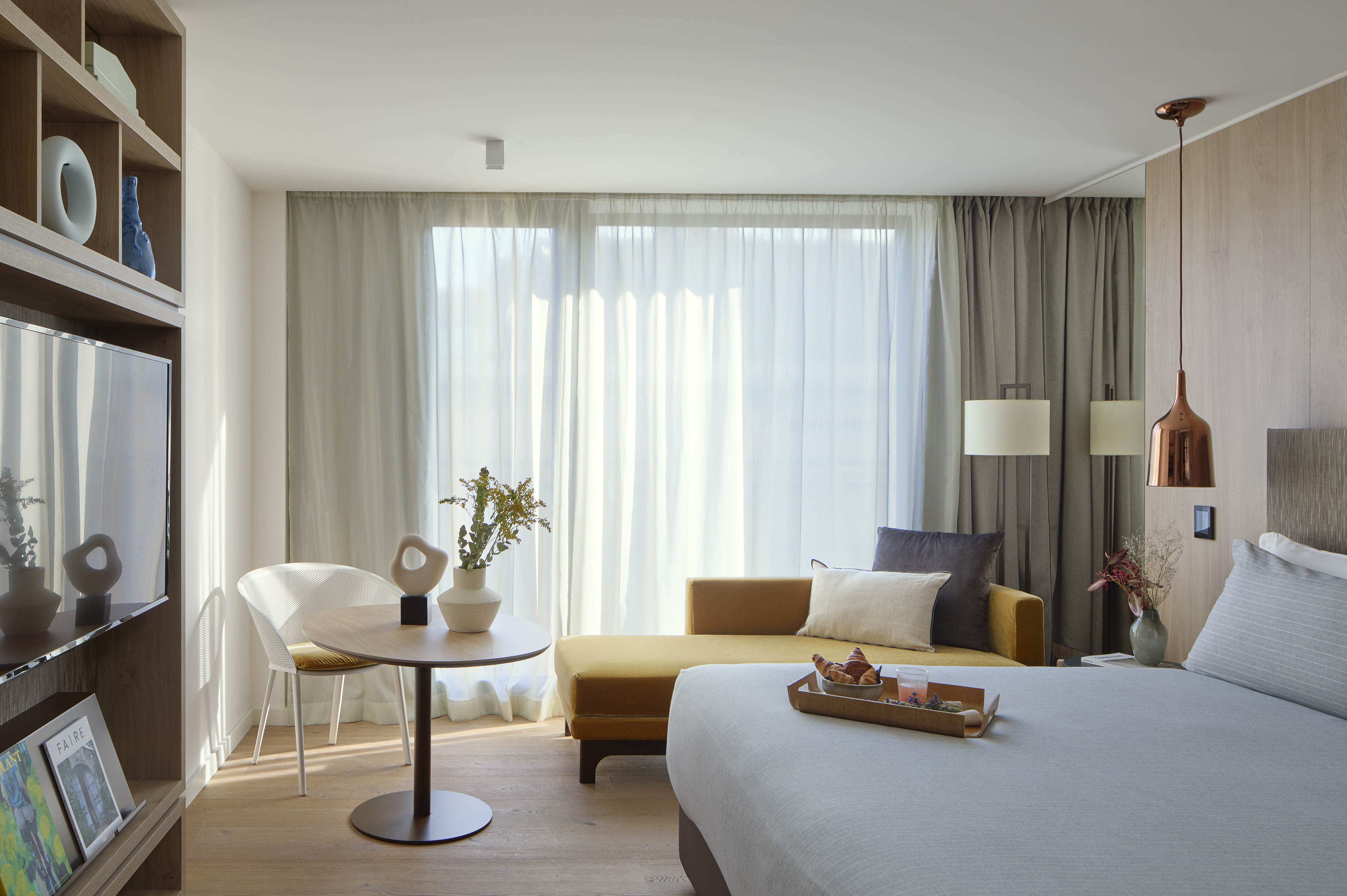 Modern hotel bedroom with yellow sofa, breakfast tray, and bright window.