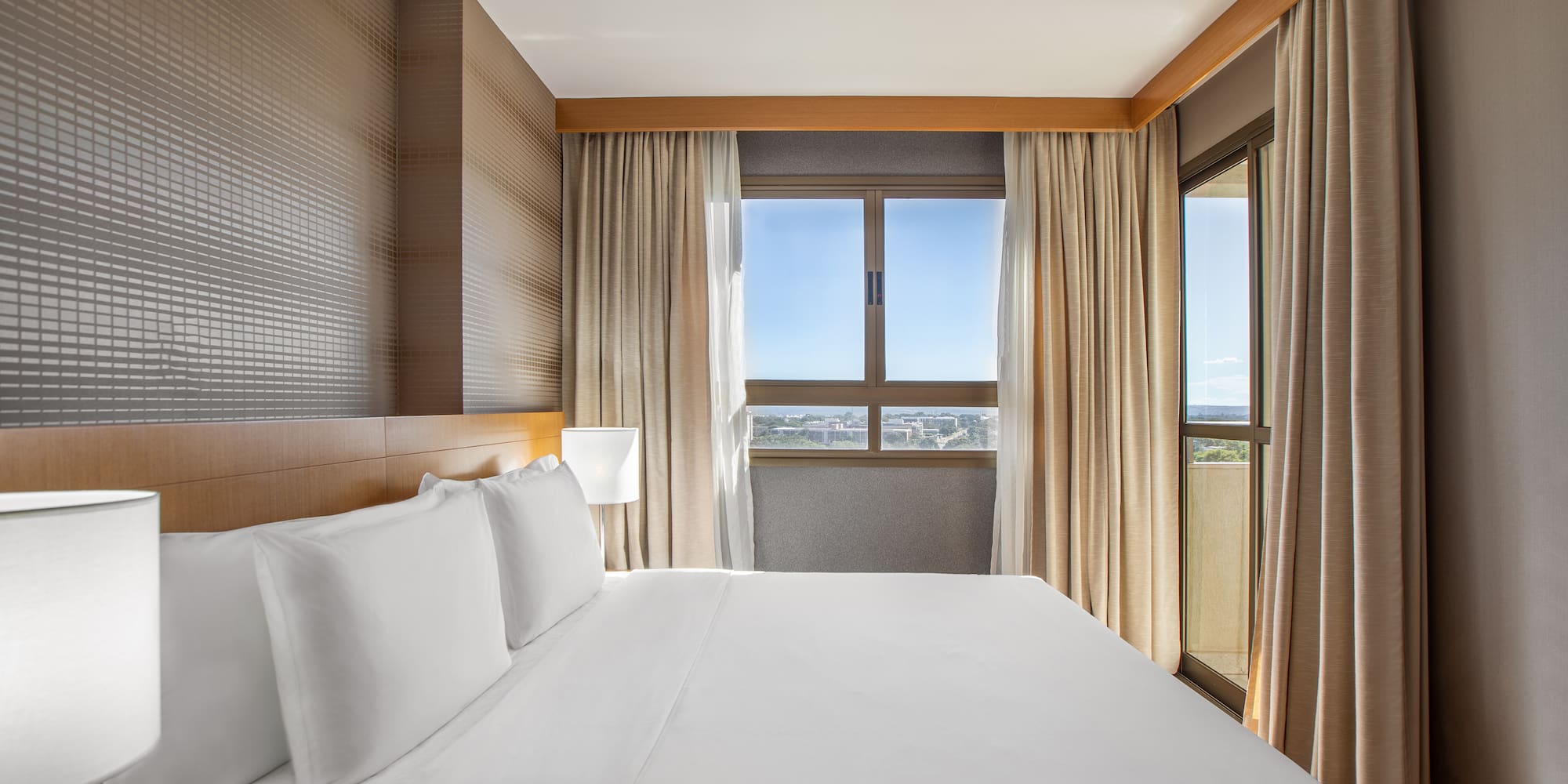 a bed with white sheets and a lamp in a room with windows