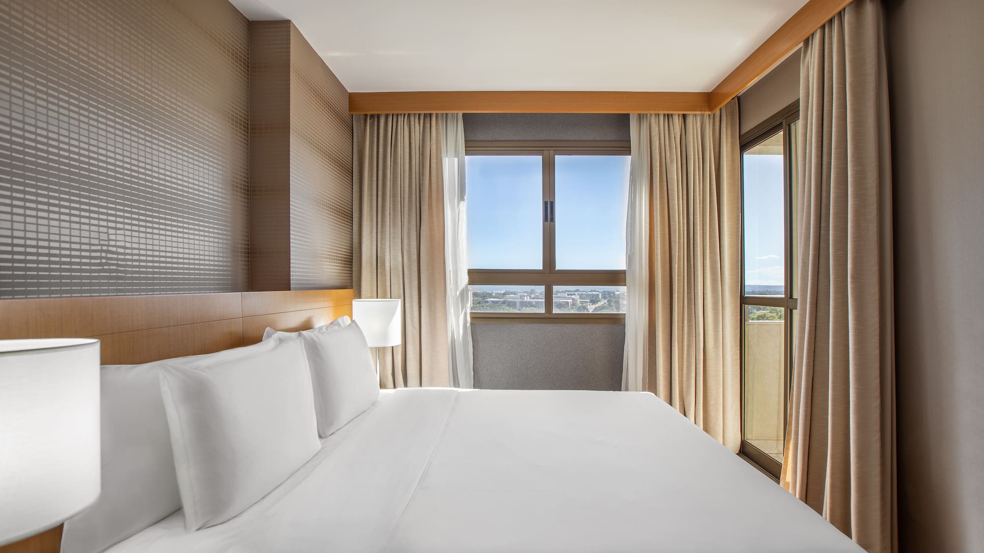 a bed with white sheets and a lamp in a room with windows