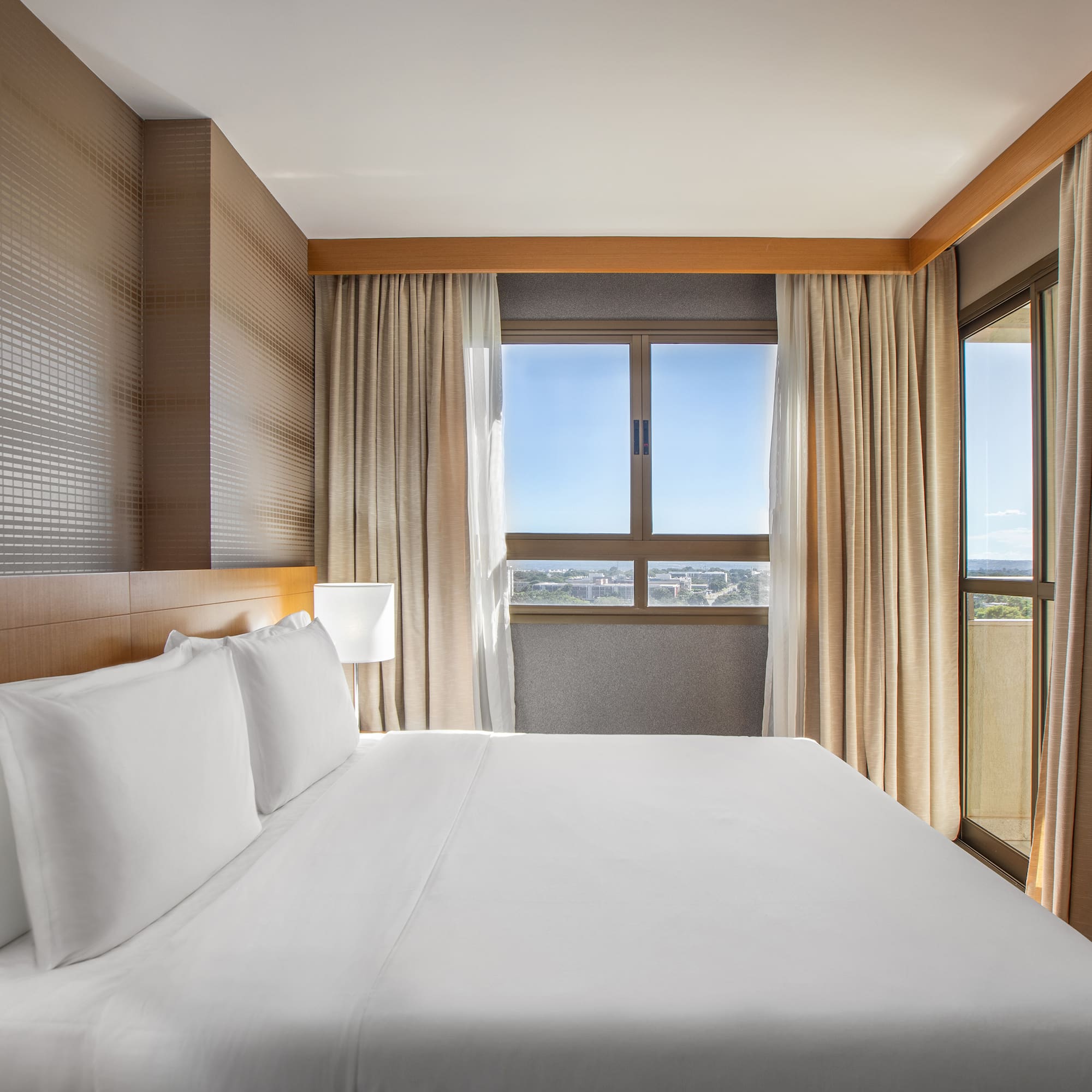 a bed with white sheets and a lamp in a room with windows