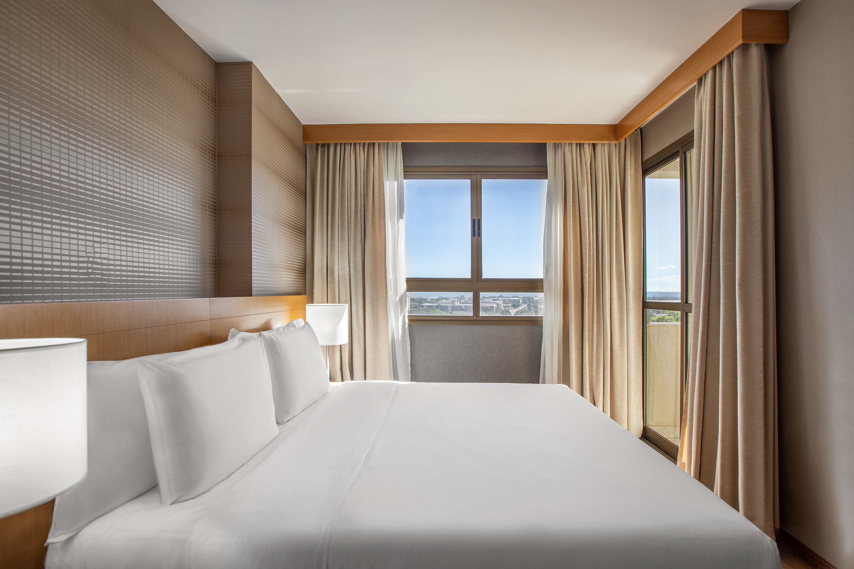 a bed with white sheets and a lamp in a room with windows