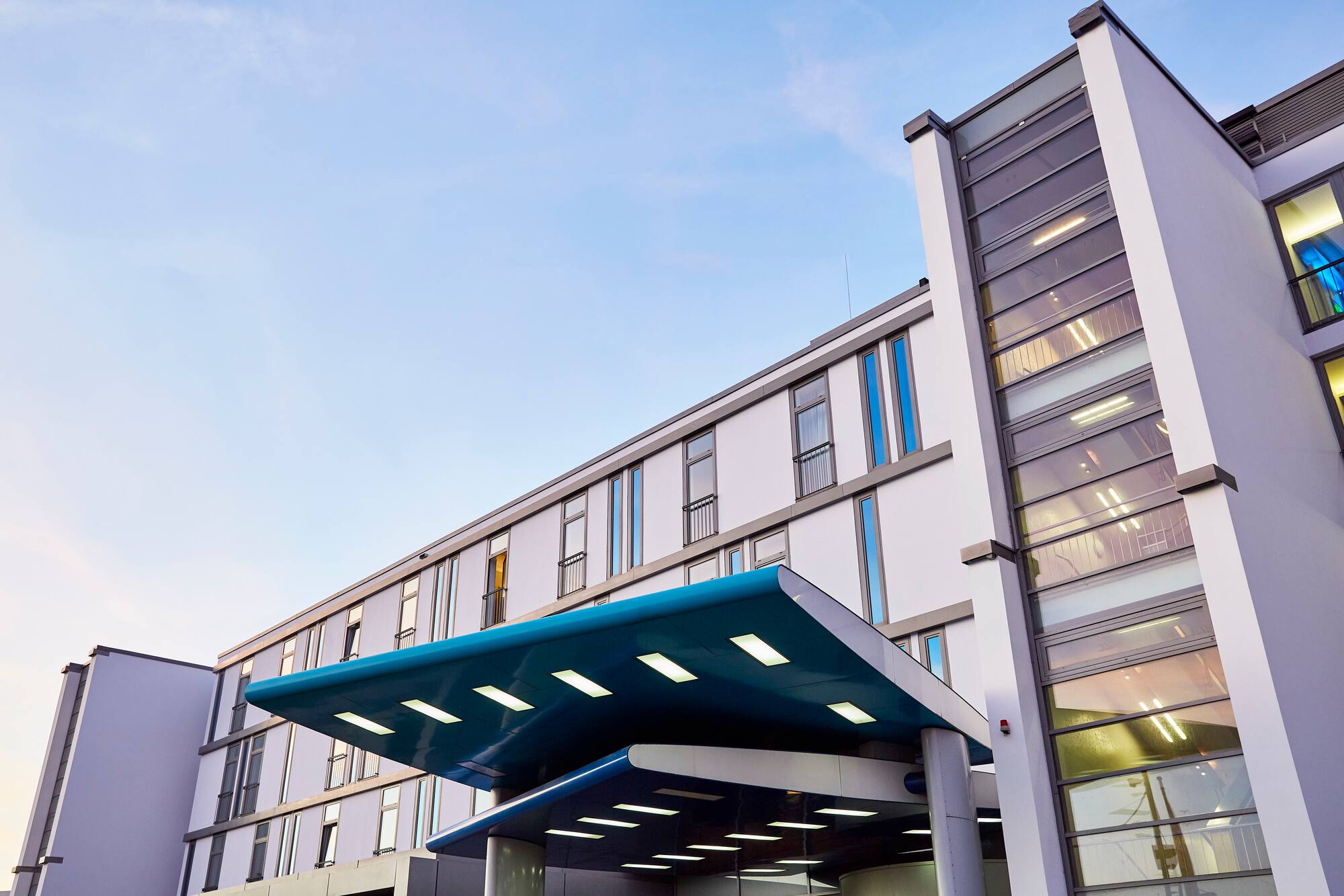 Modern hotel building exterior with blue canopy entrance under clear sky.