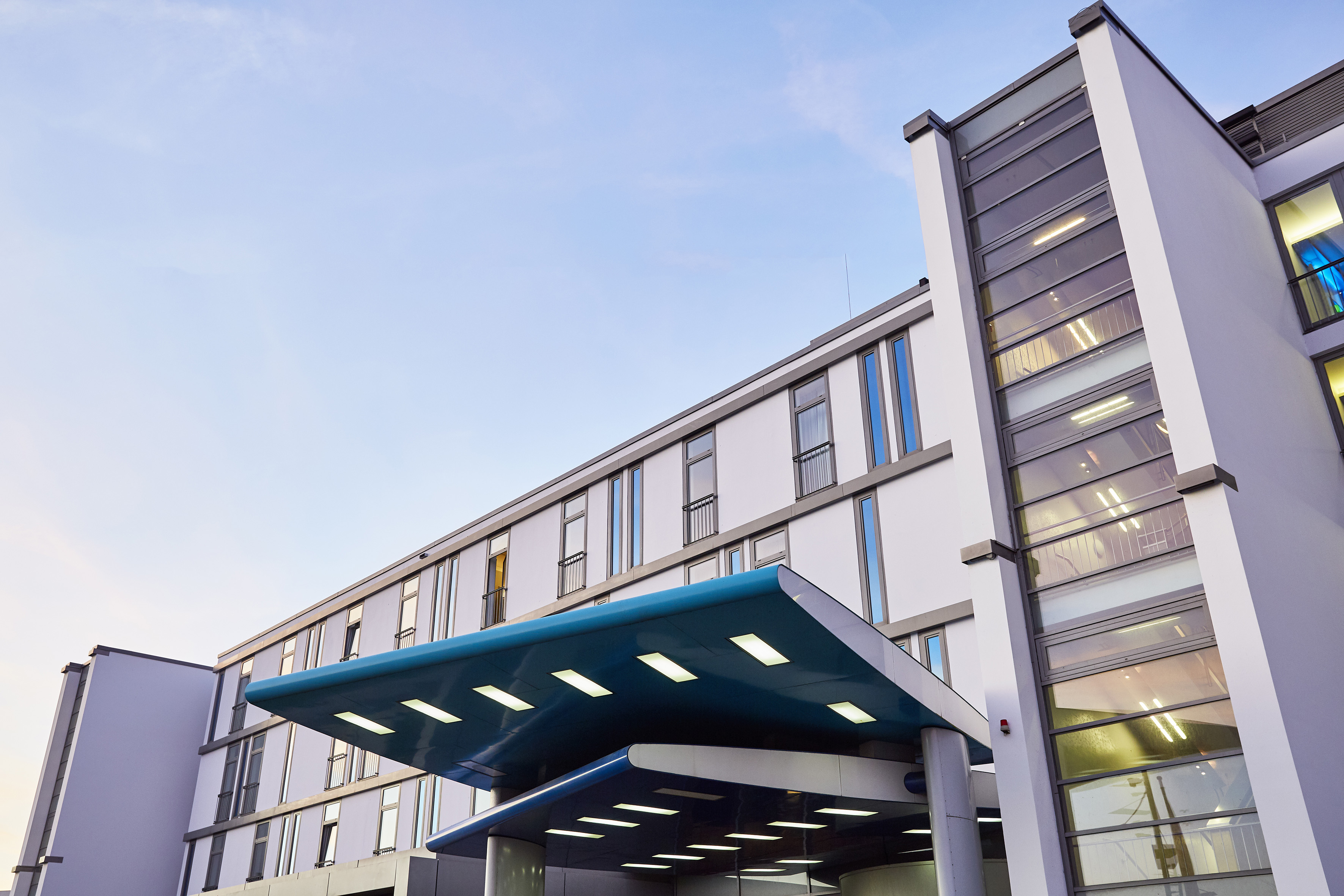Modern hotel building exterior with blue canopy entrance under clear sky.