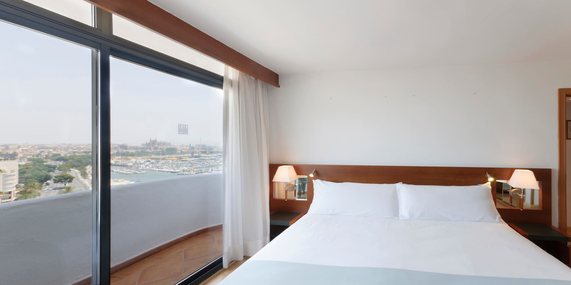a bed with white sheets and a lamp next to a glass door
