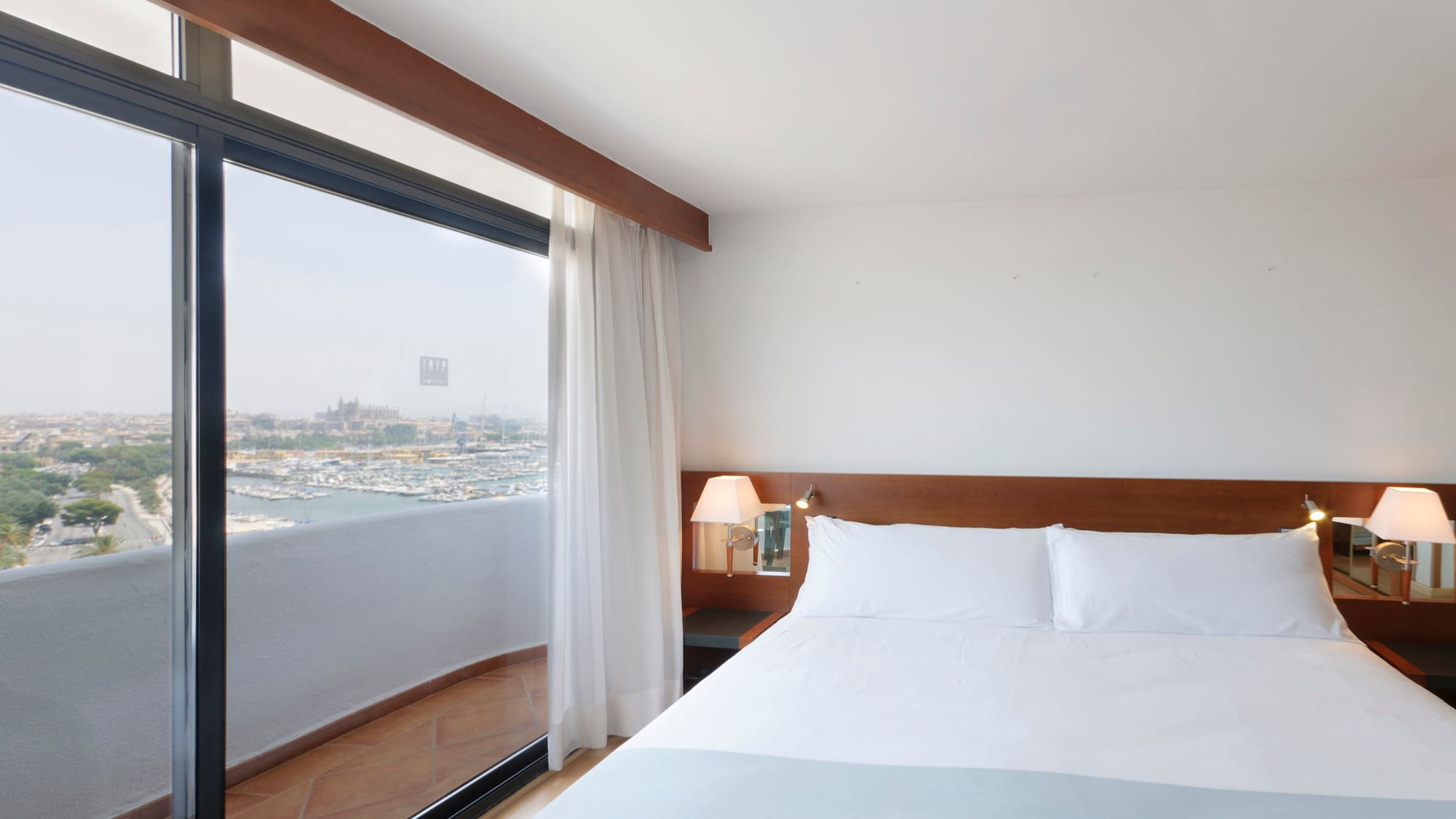 a bed with white sheets and a lamp next to a glass door