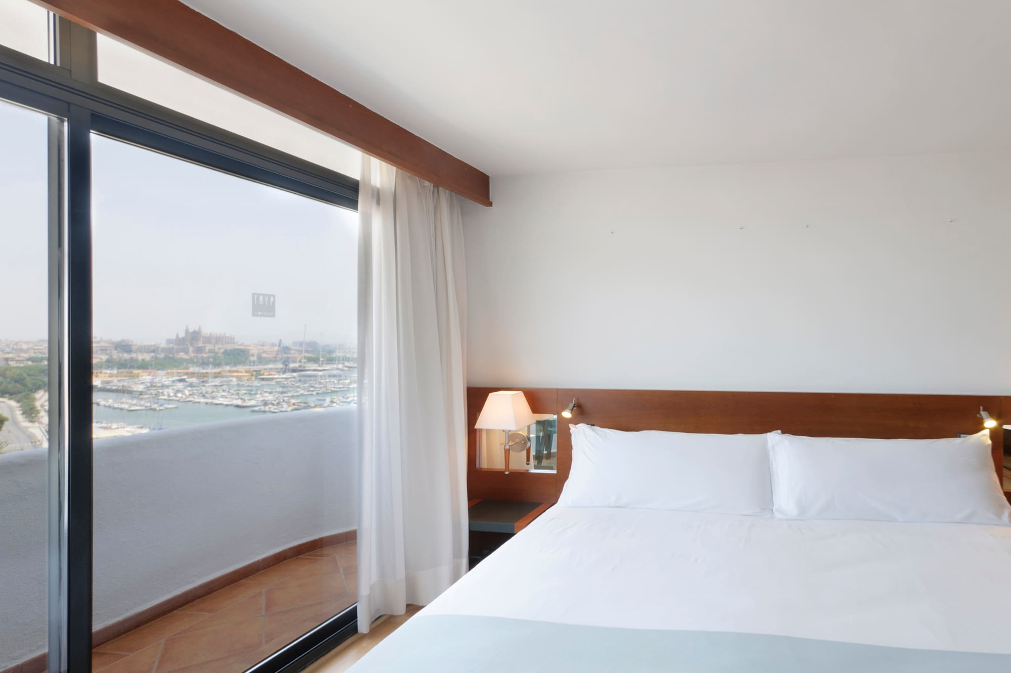 a bed with white sheets and a lamp next to a glass door