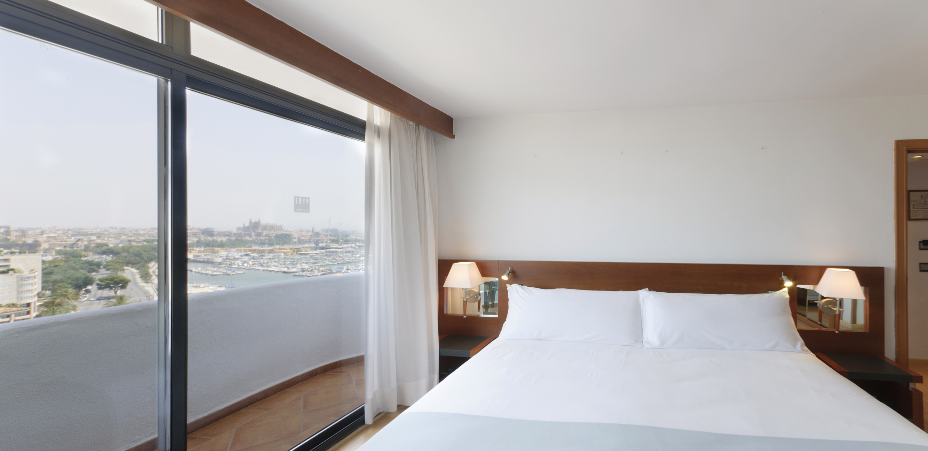 a bed with white sheets and a lamp next to a glass door