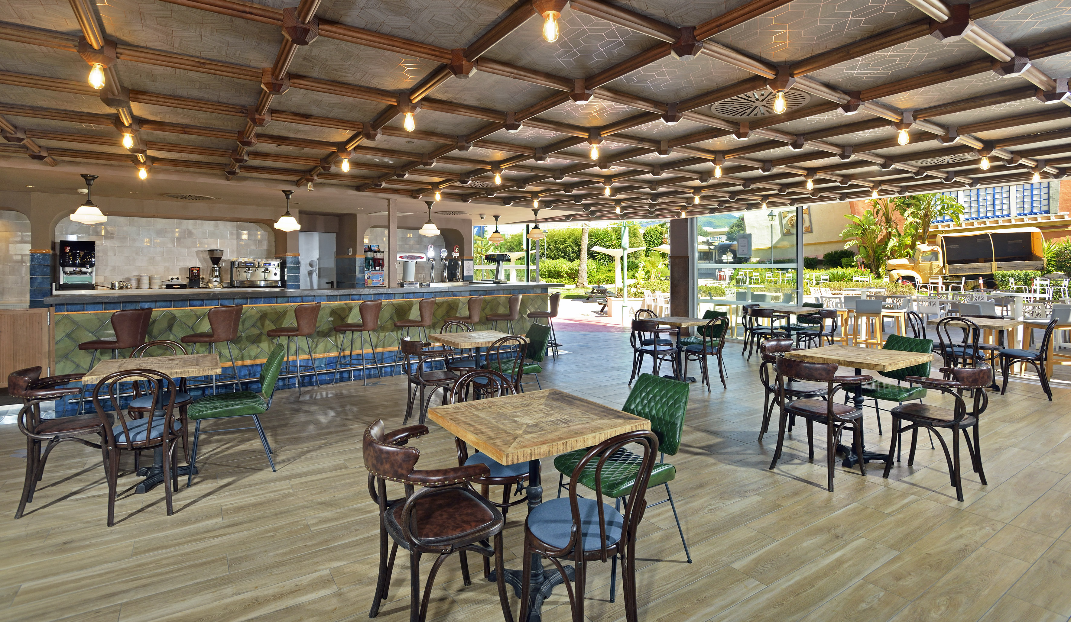Restaurant bar with wooden tables, patterned ceiling, and outdoor garden view.