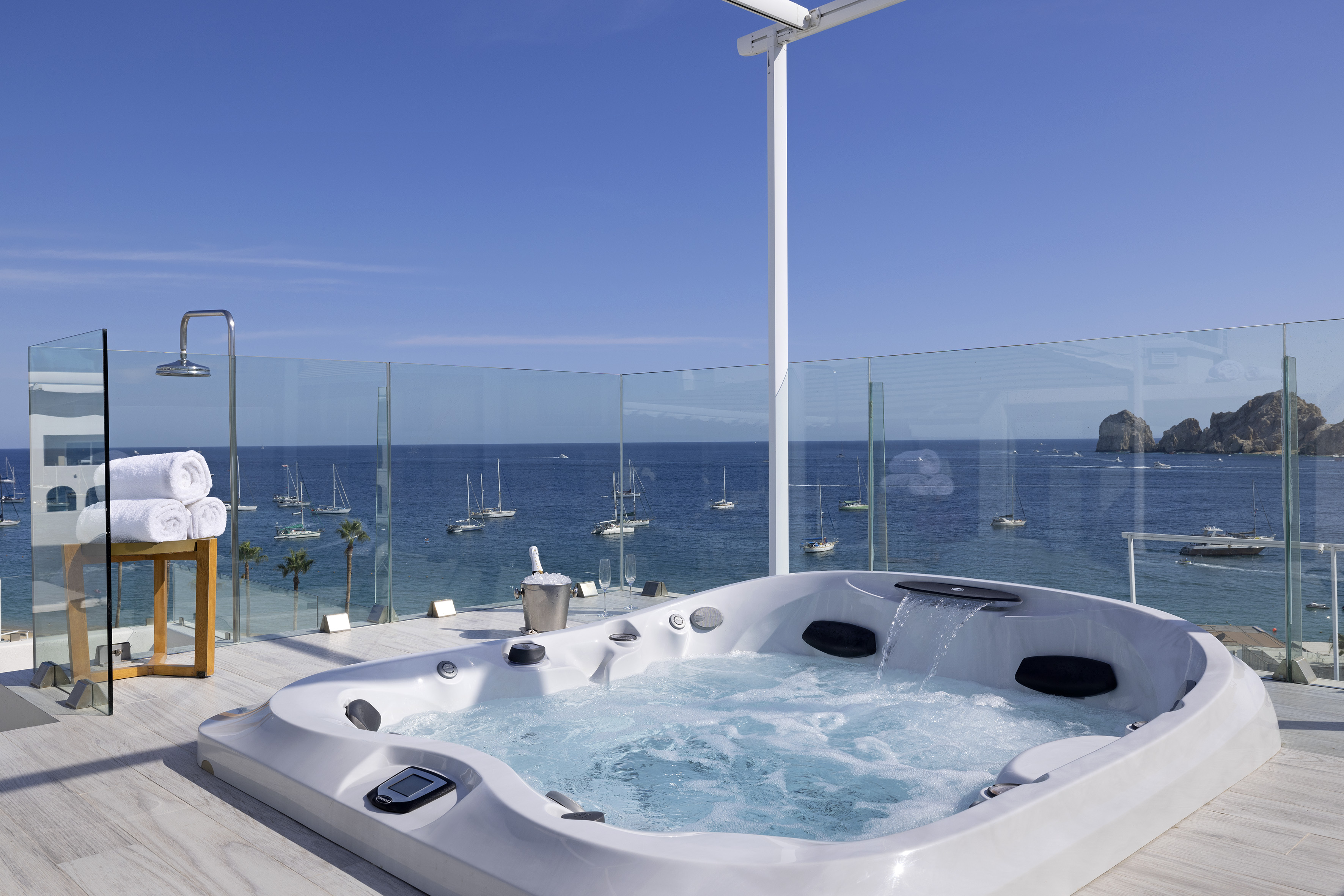 Luxury oceanfront hot tub on a terrace with sailboats and rocky islands.