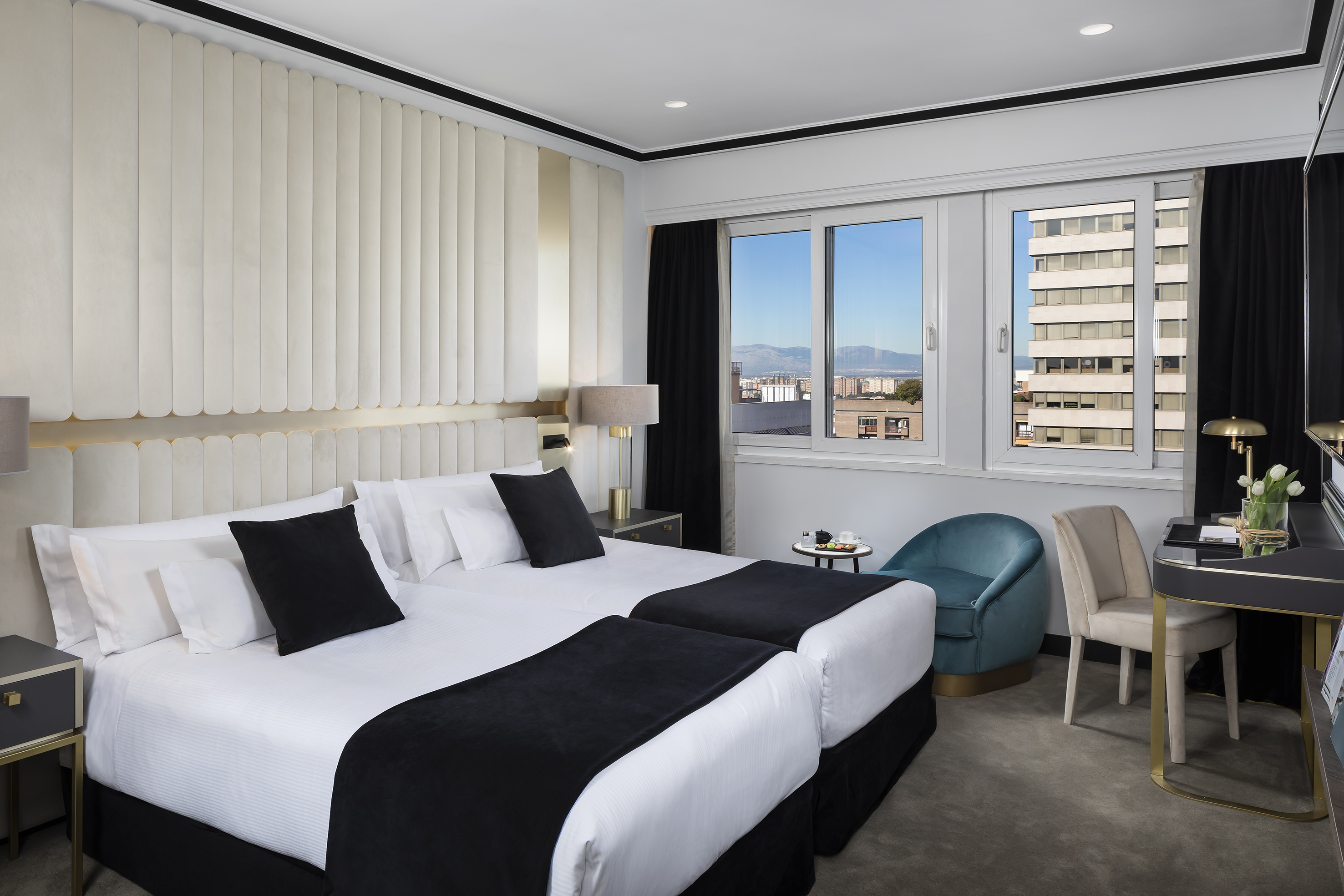 Modern hotel room with twin beds, city view, and sleek contemporary decor.