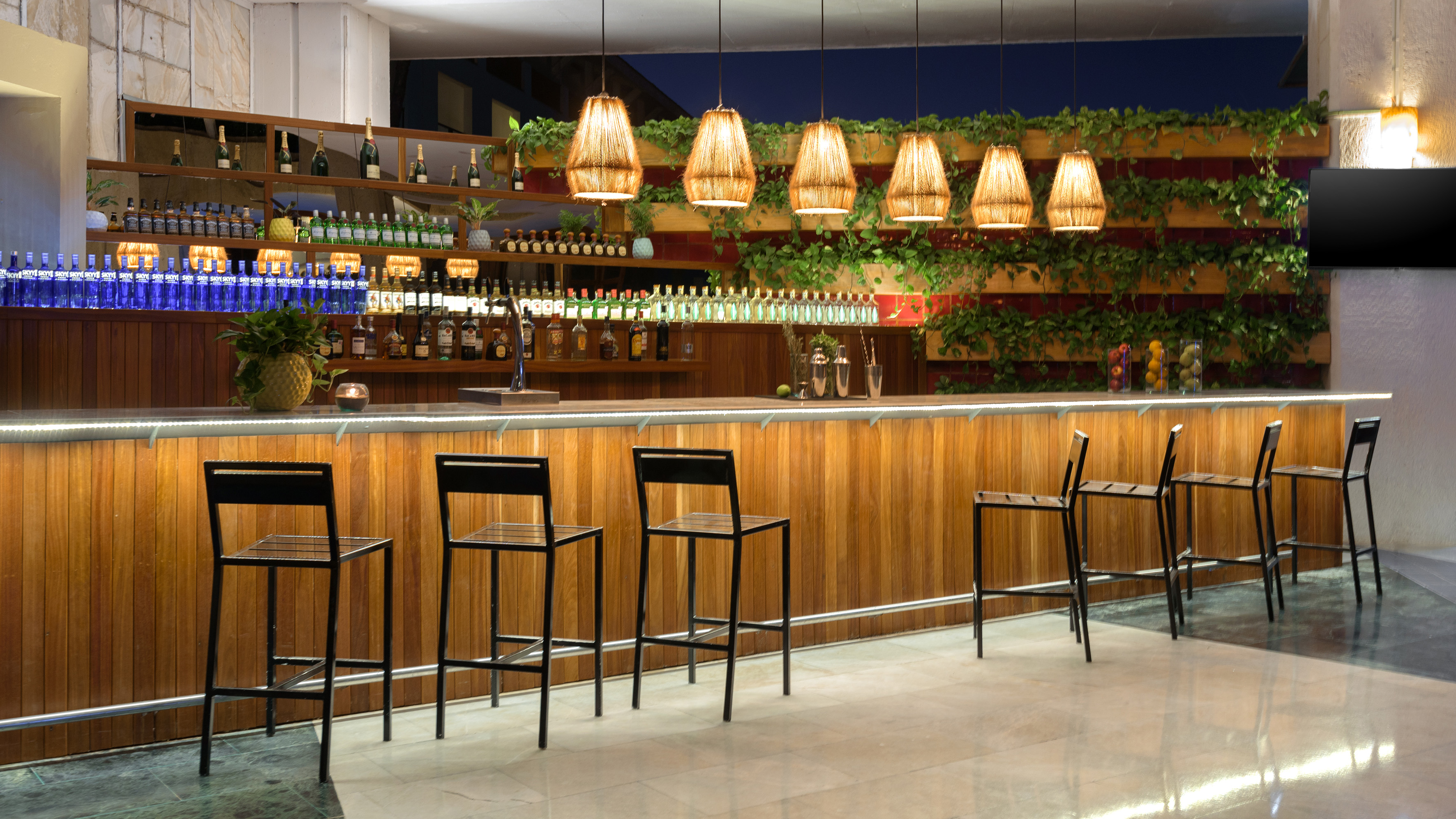Modern wood bar with spirits, bar stools, pendant lighting, and plant decor.