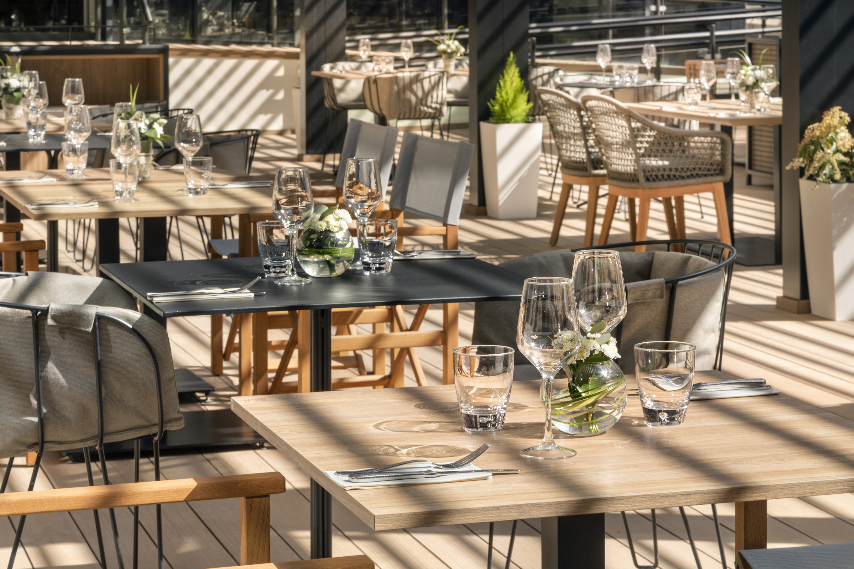 Al fresco restaurant terrace with set tables, glassware, and sunlit wood deck.