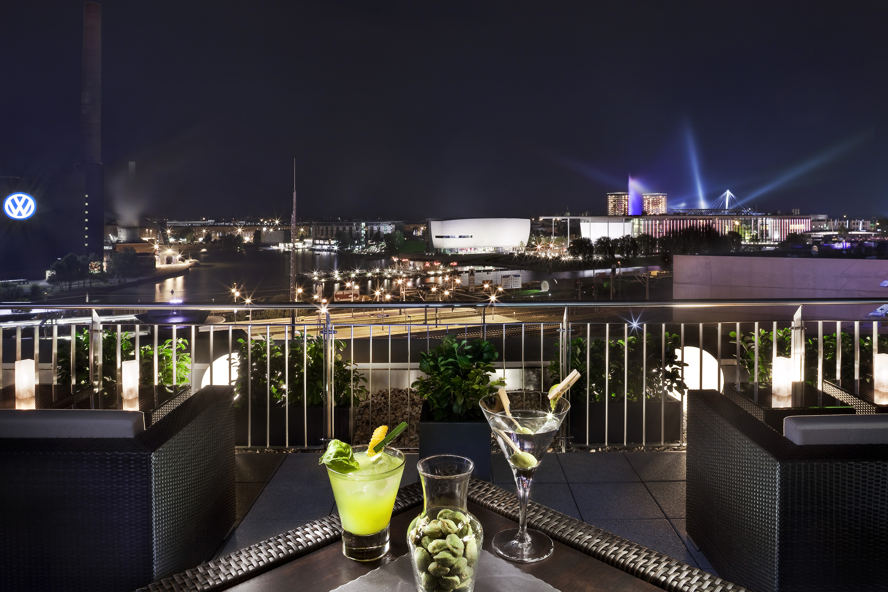 Night city skyline from rooftop bar with cocktails and prominent VW logo.