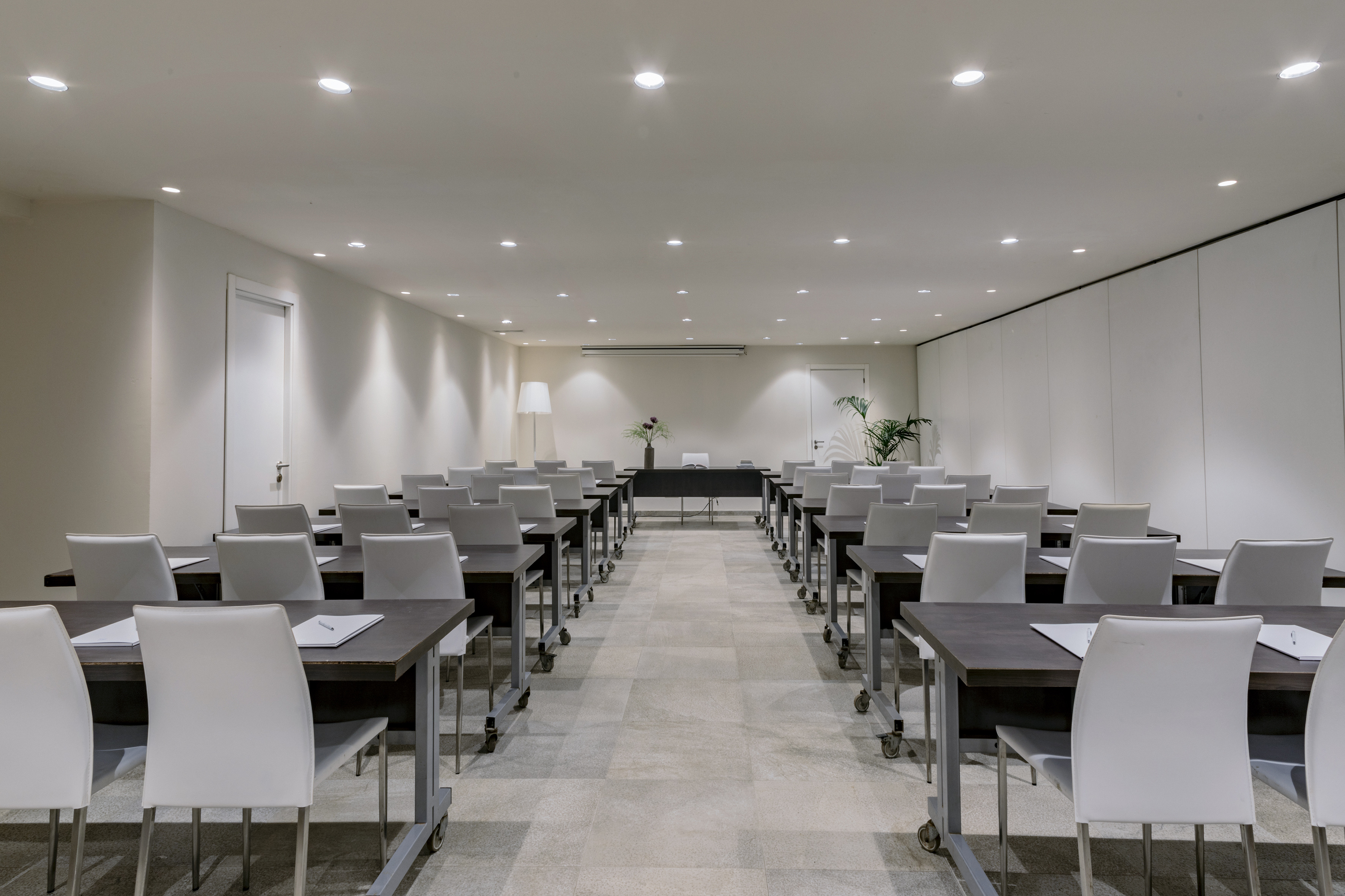 Empty conference room with seminar setup, dark tables, and white chairs.