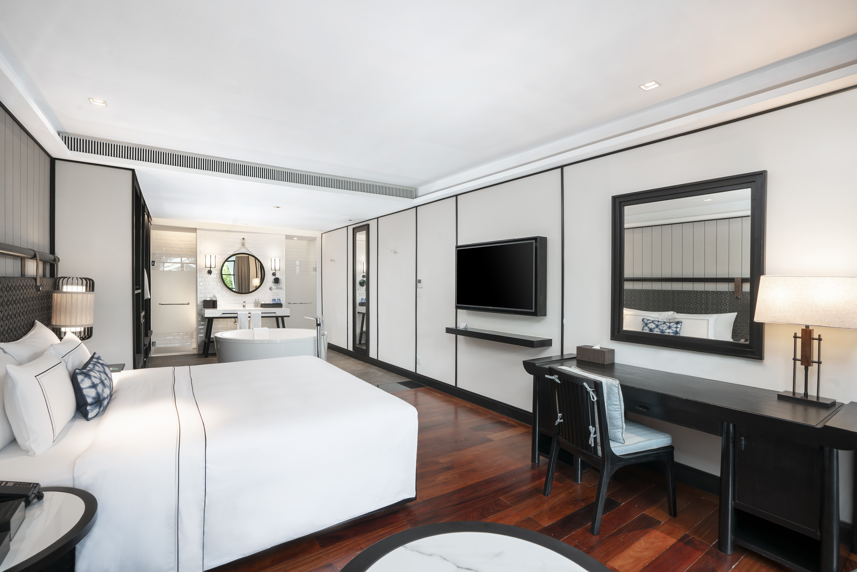 Modern luxury hotel room with king bed, desk, TV, and open spa bathroom.