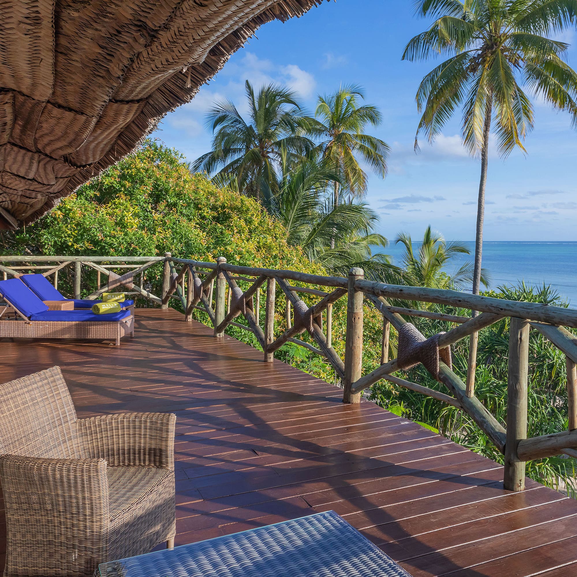 a deck with chairs and a thatched roof overlooking the ocean