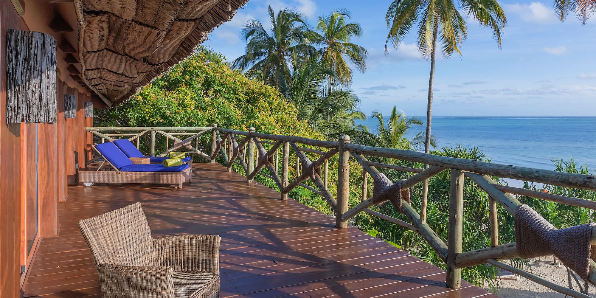 a deck with chairs and a thatched roof overlooking the ocean