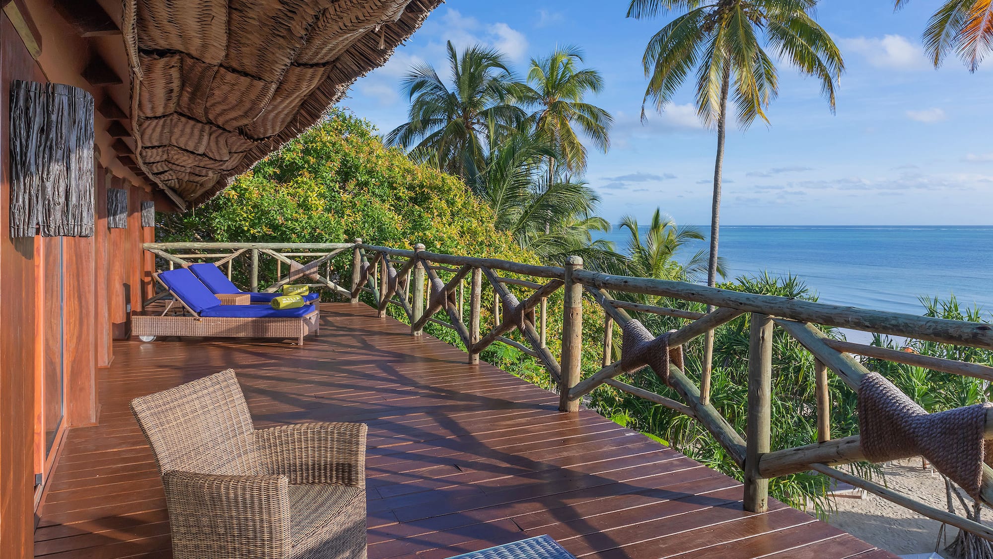 a deck with chairs and a thatched roof overlooking the ocean