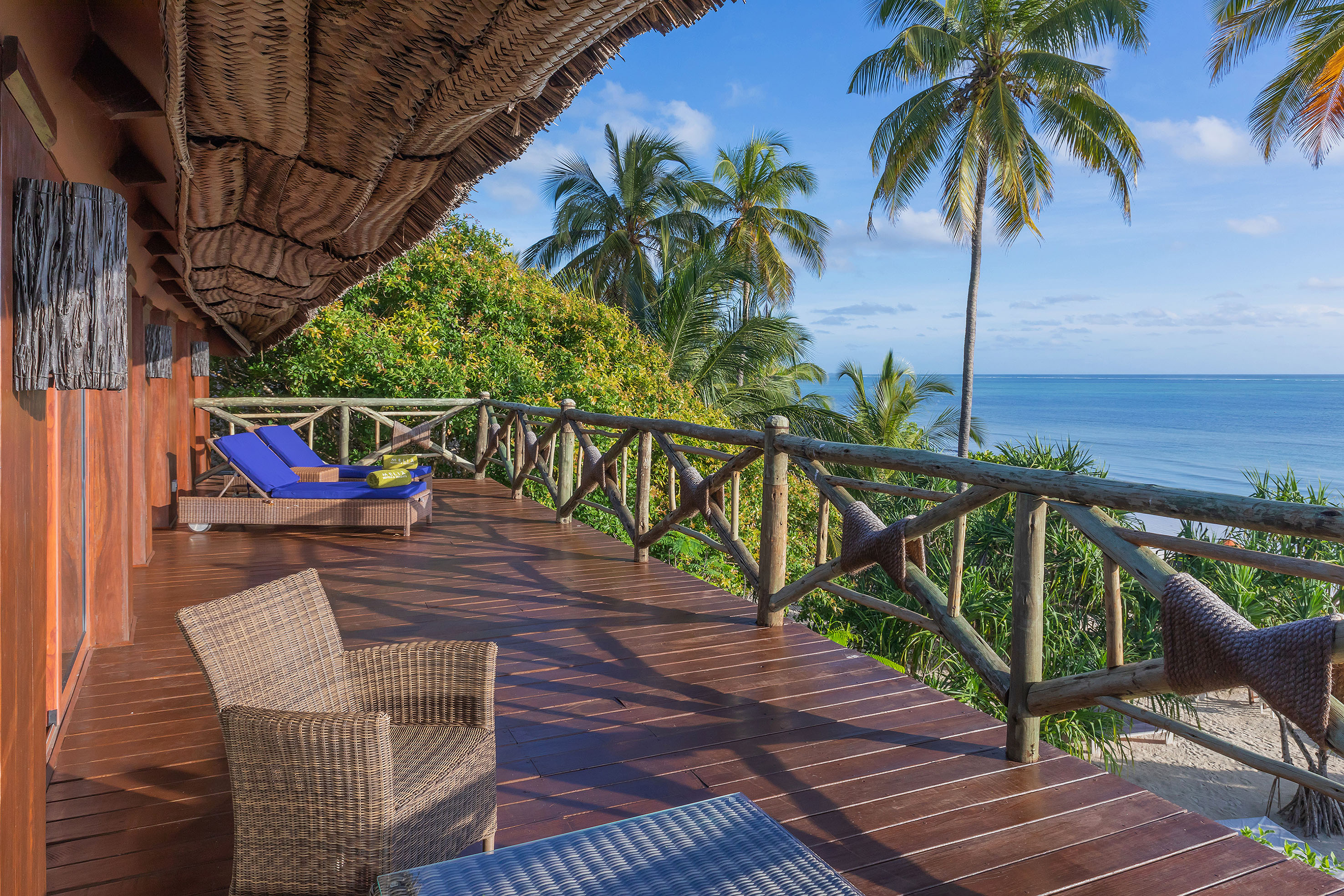 Ocean view deck with palm trees, wicker furniture, and thatch roof.