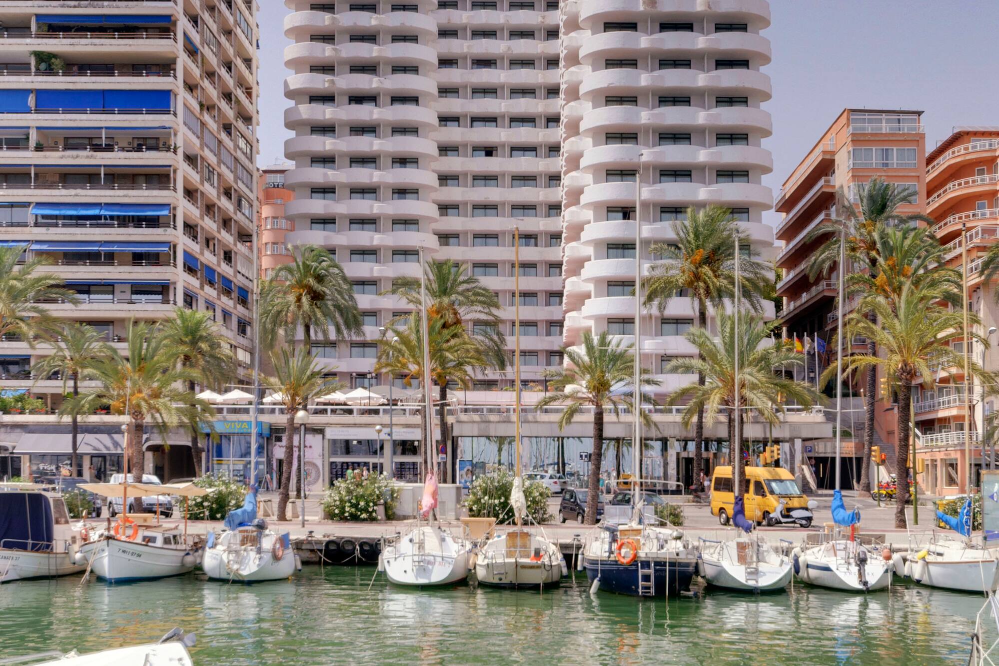 Marina with boats, palm trees, and Hotel Palma Bellver in Palma de Mallorca.
