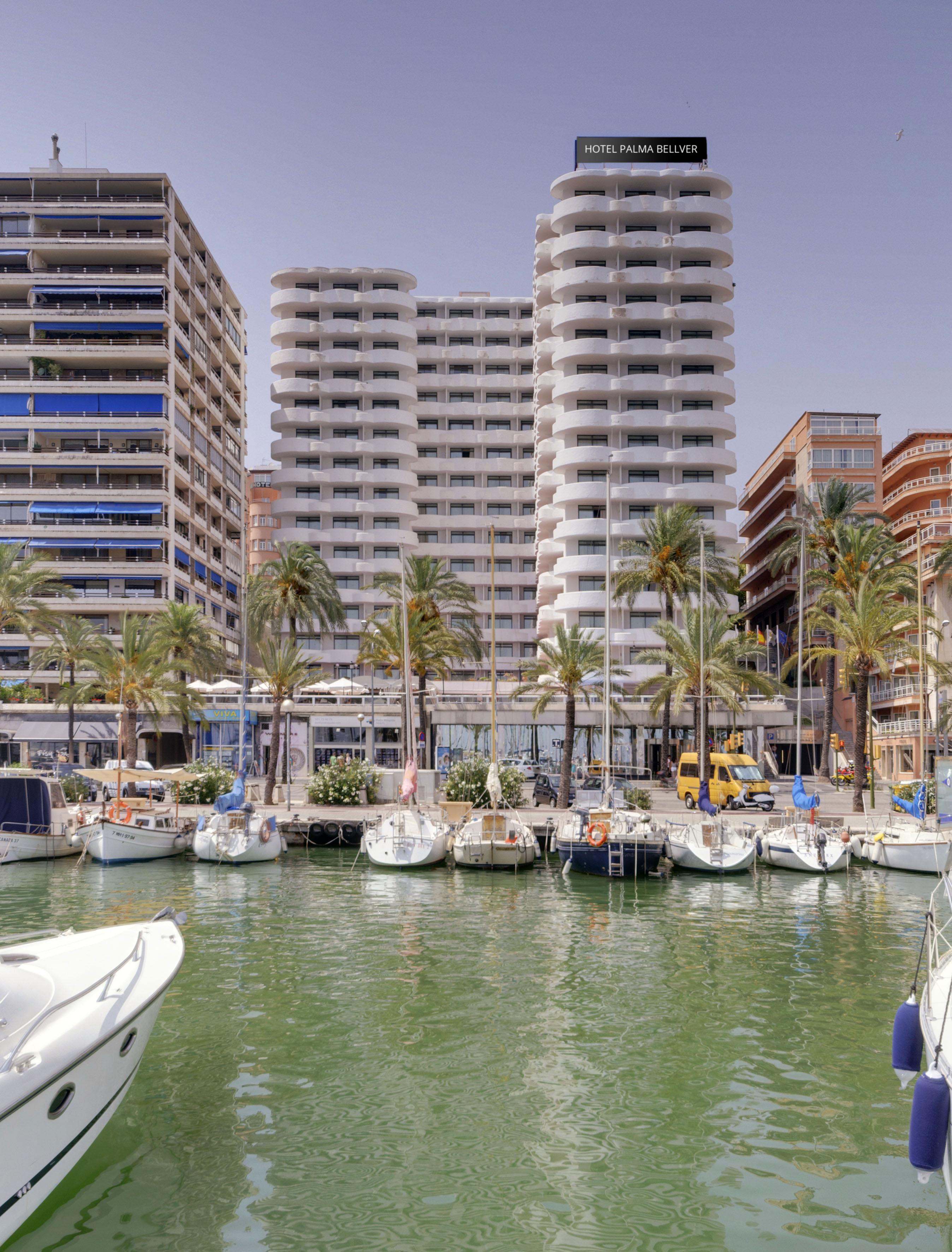 Marina with boats, palm trees, and Hotel Palma Bellver in Palma de Mallorca.