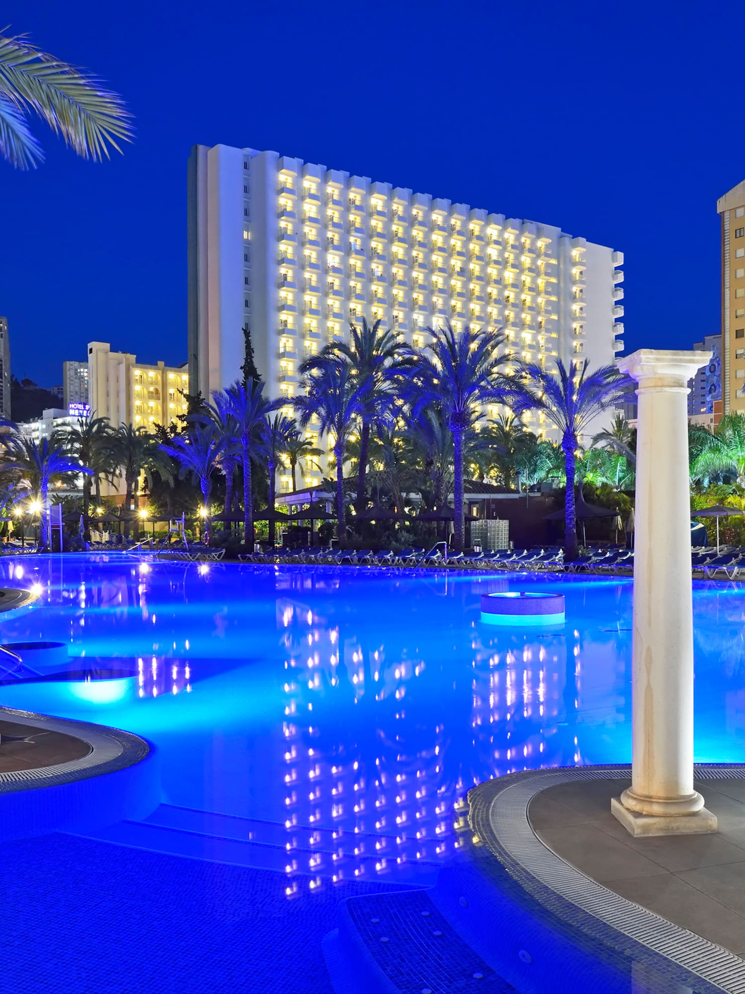 a pool with columns and palm trees in the background
