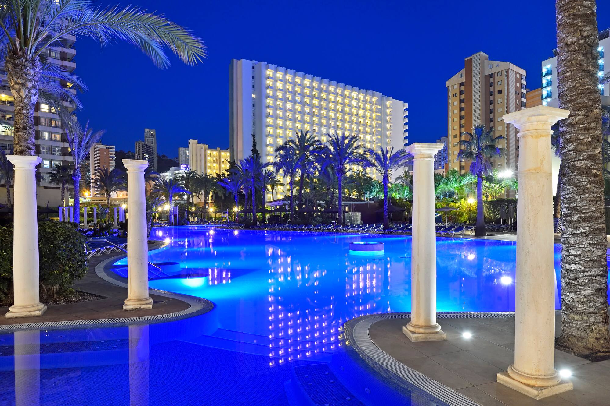 a pool with columns and palm trees in the background