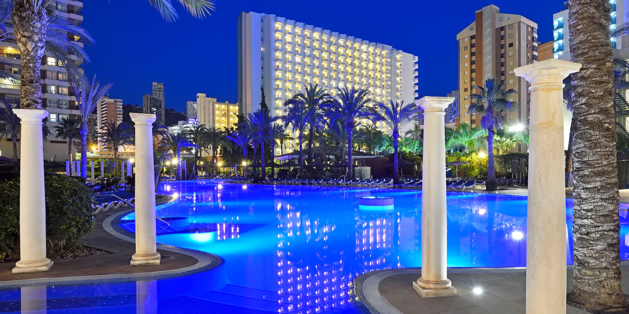 a pool with columns and palm trees in the background