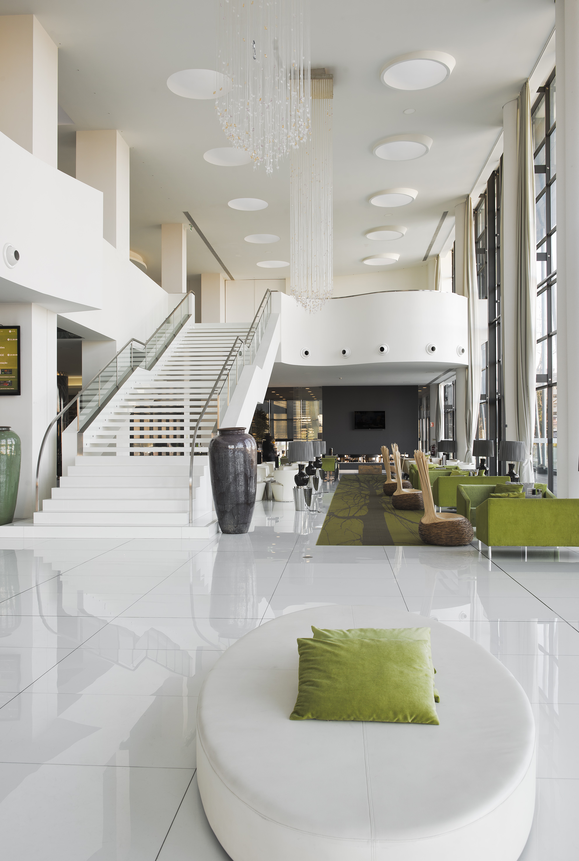 Bright hotel lobby with white staircase, crystal chandelier, and green seating.