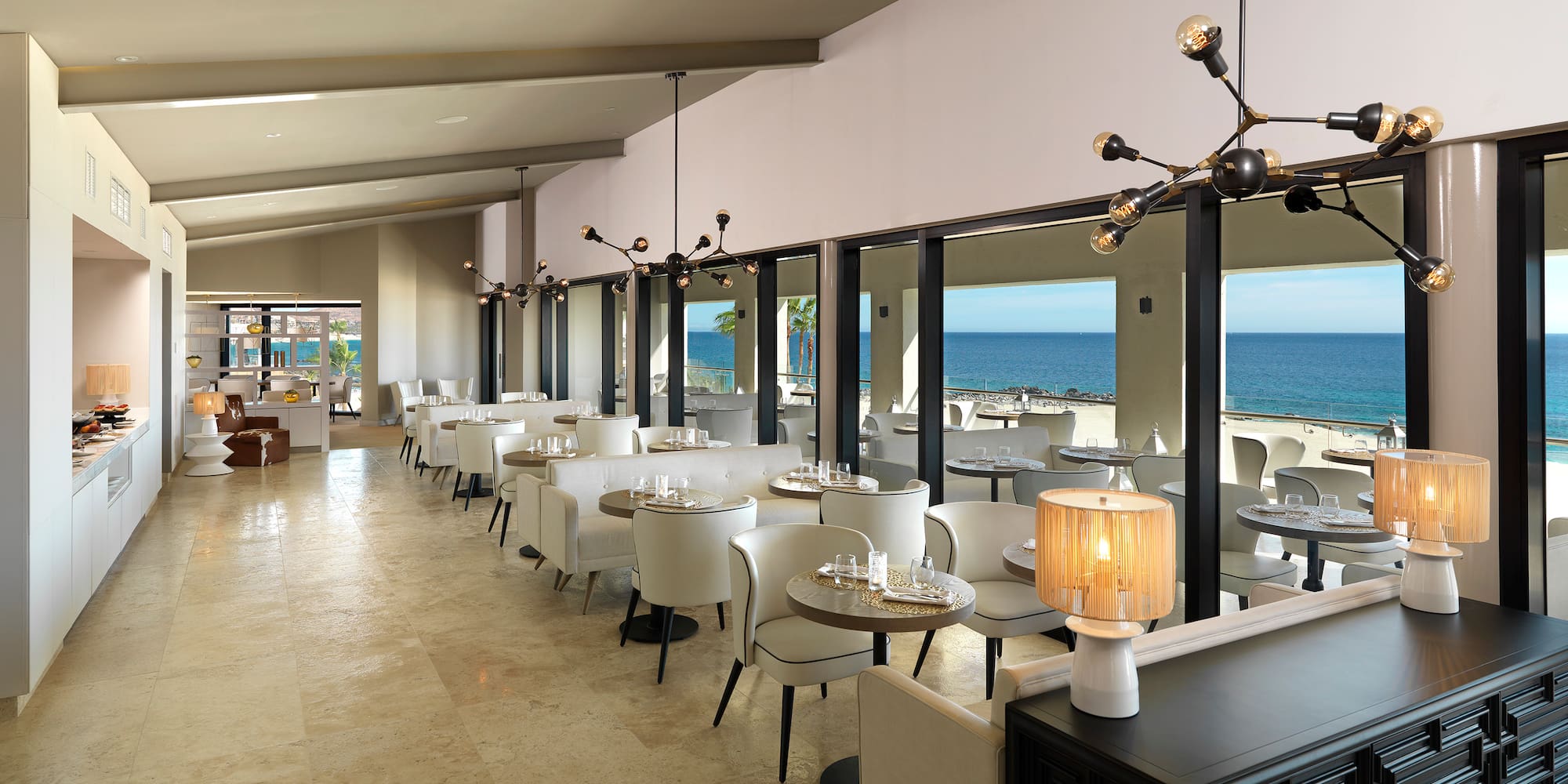 a room with tables and chairs and a view of the ocean