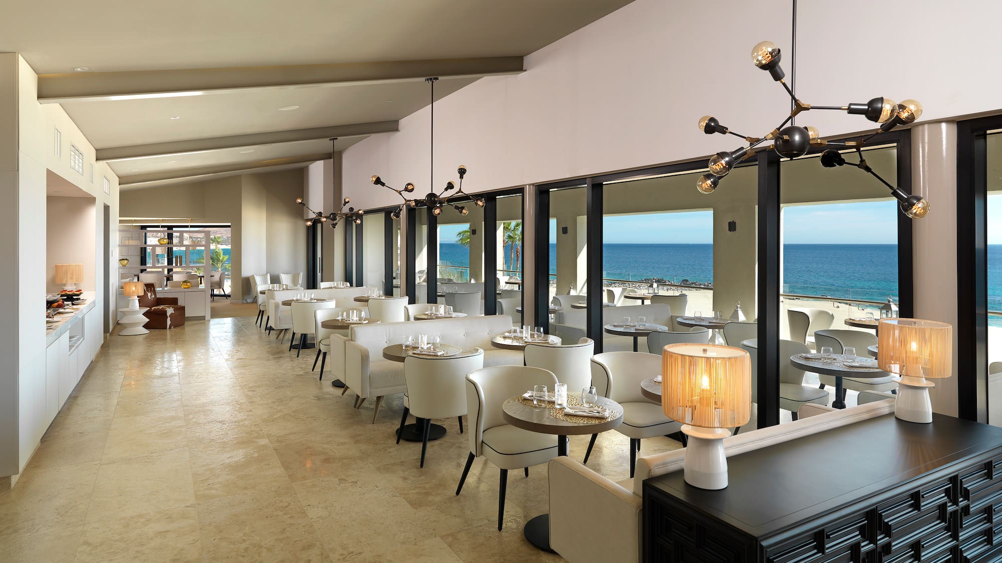 a room with tables and chairs and a view of the ocean