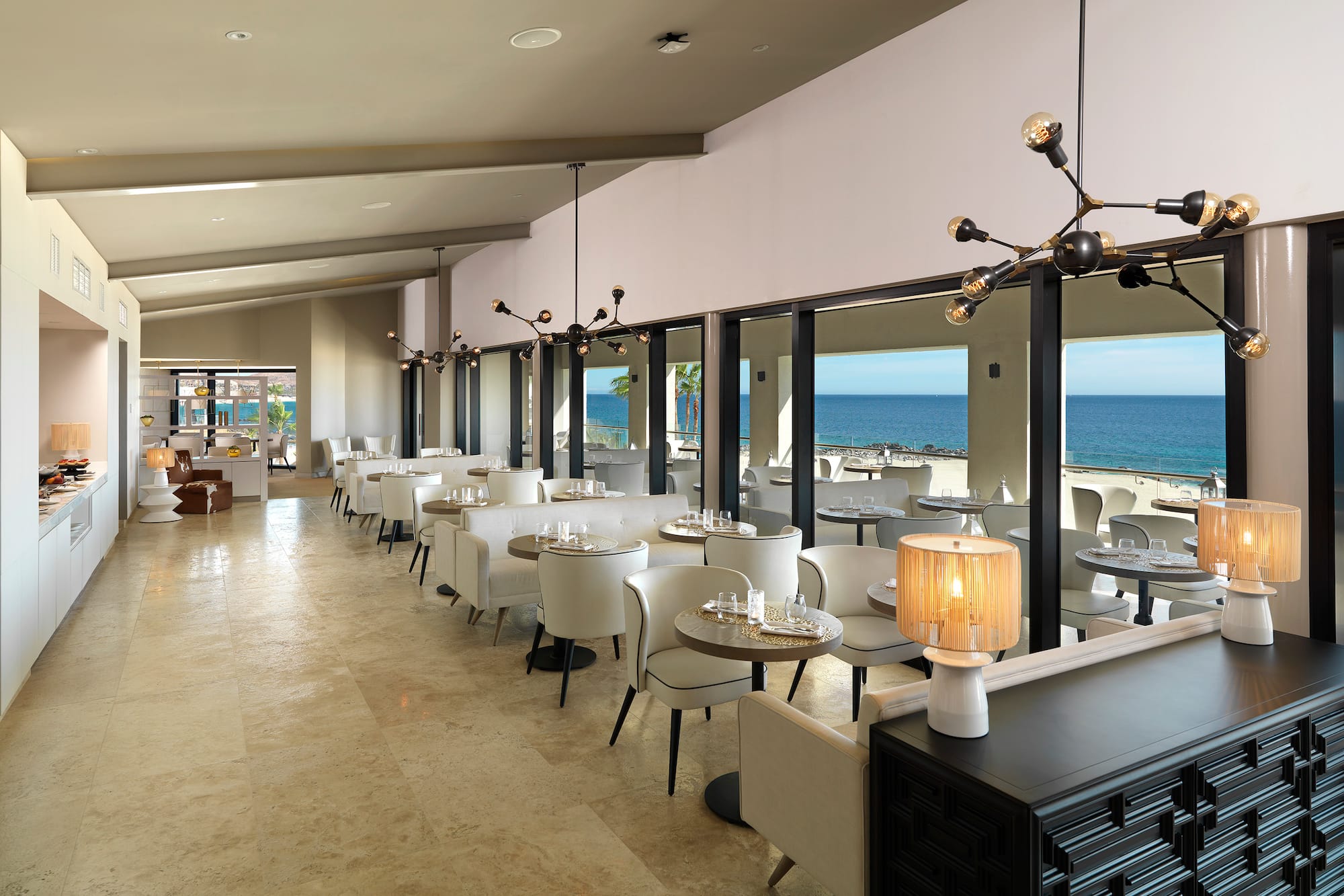 a room with tables and chairs and a view of the ocean