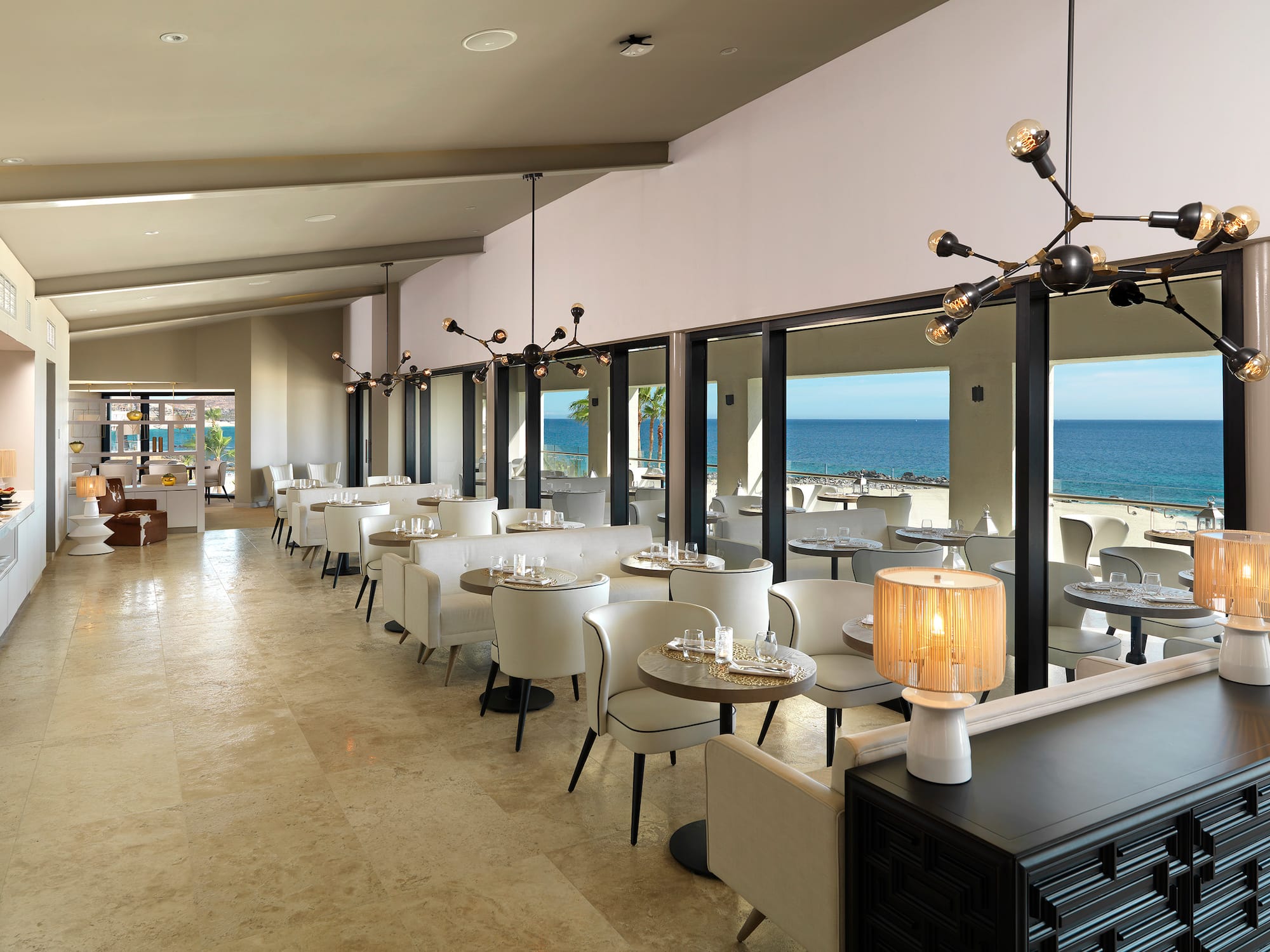a room with tables and chairs and a view of the ocean