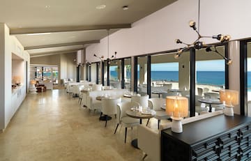 a room with tables and chairs and a view of the ocean