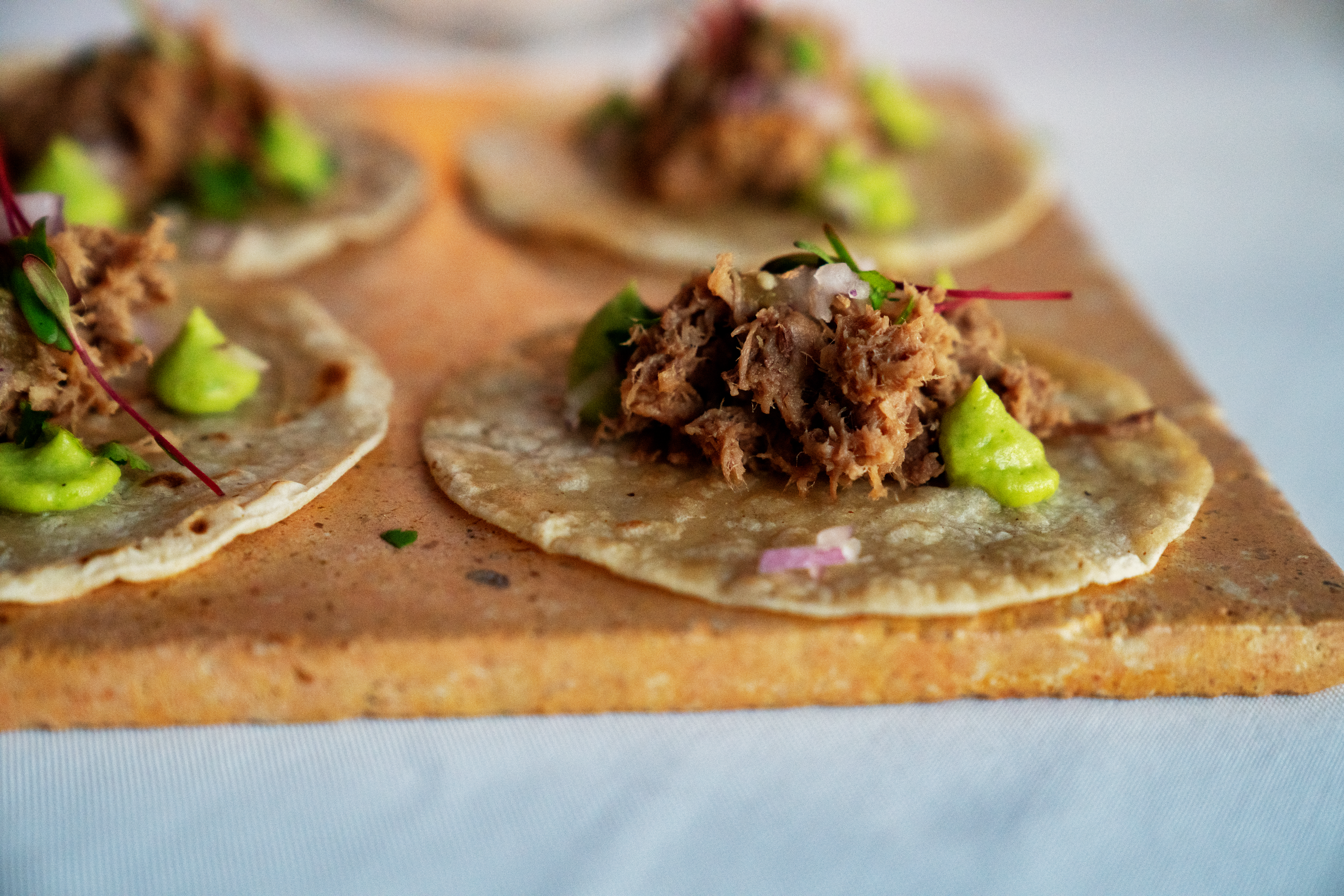 Tacos con carne deshebrada, aguacate y cebolla morada en tabla.